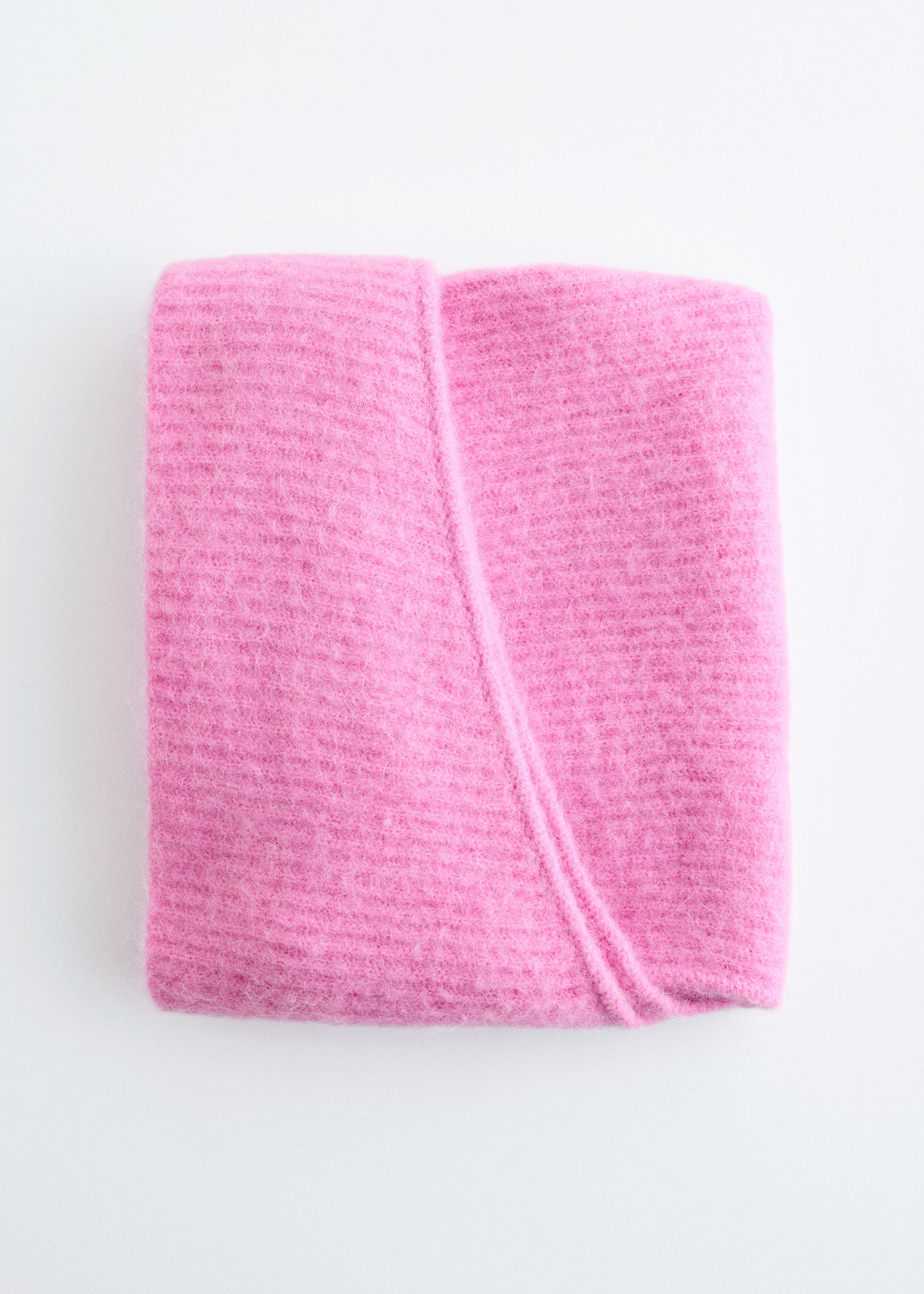 Se større billede: En pink sweater viser en fluffy, børstet tekstur med subtile horisontale striklinjer, pænt foldet i en rektangulær form med en distinkt diagonal fold hen over dens øverste overflade.