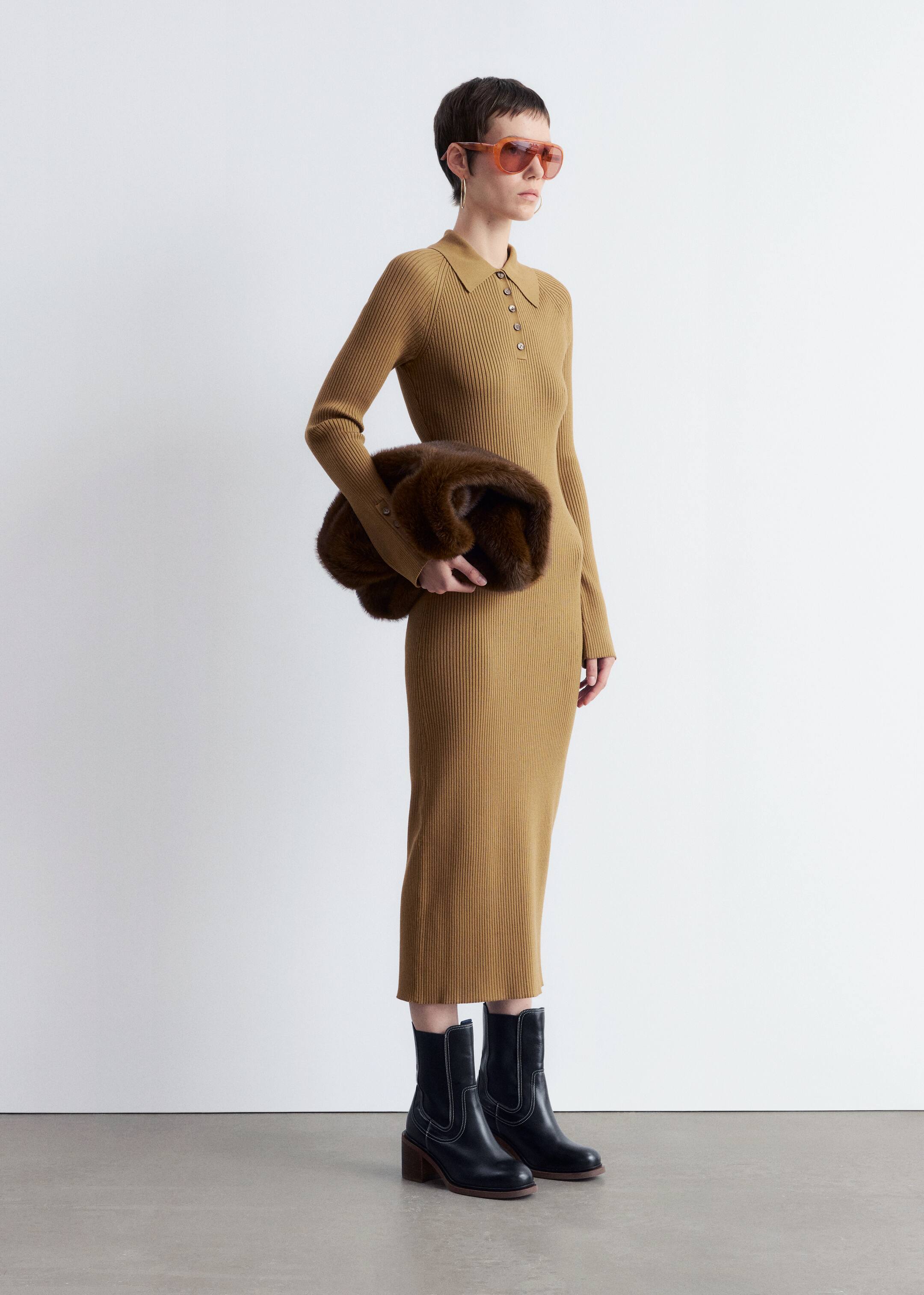 Agrandir l'image: Une longue robe en maille côtelée de couleur camel est présentée sous un léger angle latéral, avec un col polo doté d'une patte de boutonnage à trois boutons et de longues manches ajustées avec des poignets boutonnés.