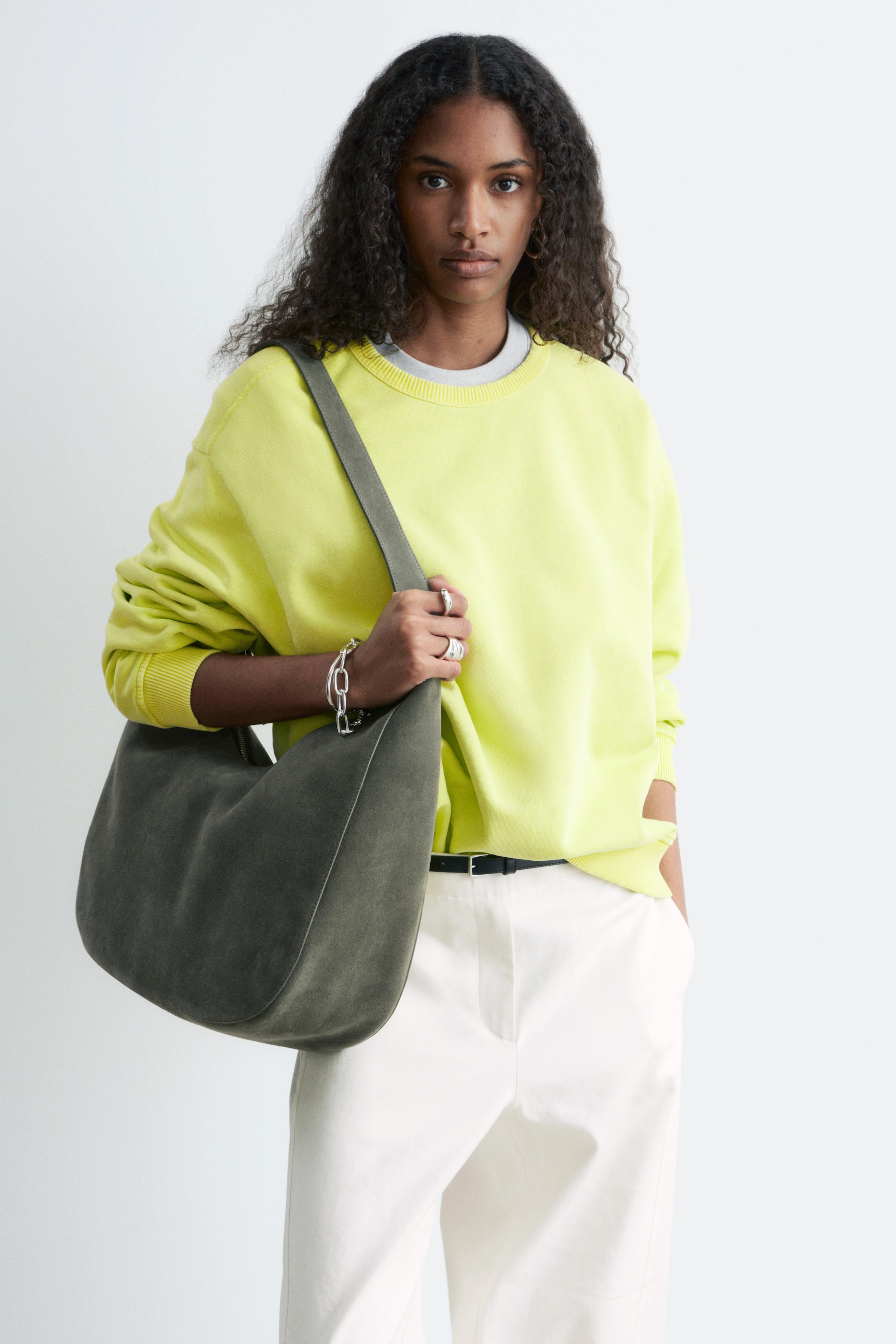 Zobacz większy obraz: Limonkowo-żółta bluza z okrągłym dekoltem prezentuje oversize'owy krój z długimi rękawami oraz prążkowanymi mankietami i dołem. Jest noszona na jasnoszarym t-shircie, widocznym przy dekolcie.