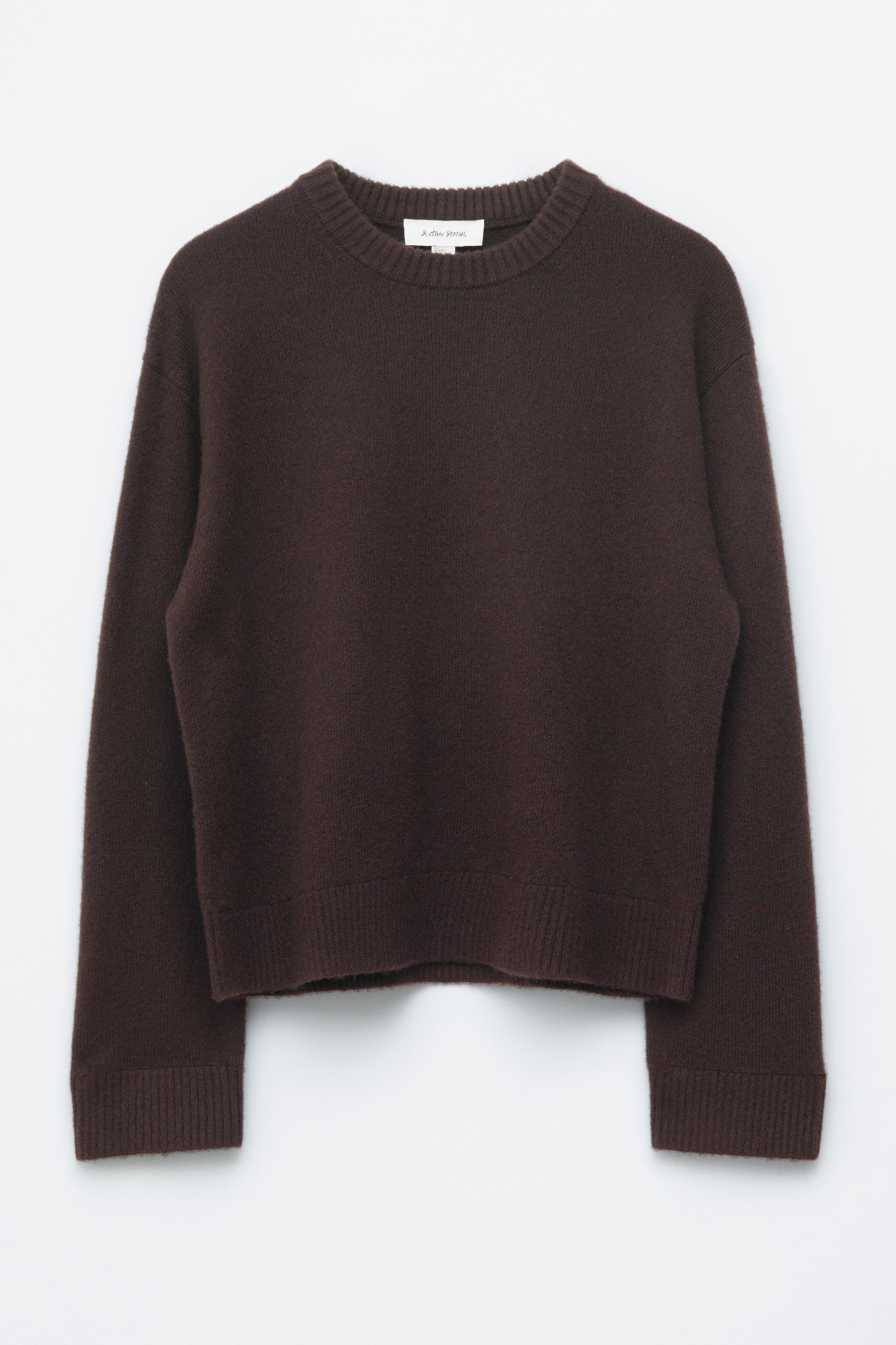 Grösseres Bild ansehen: Ein dunkelbrauner Pullover wird von vorne präsentiert, mit einer kastigen Passform und überschnittenen Schultern. Er ist mit einem gerippten Rundhalsausschnitt, gerippten Bündchen und einem gerippten Saum gestaltet.