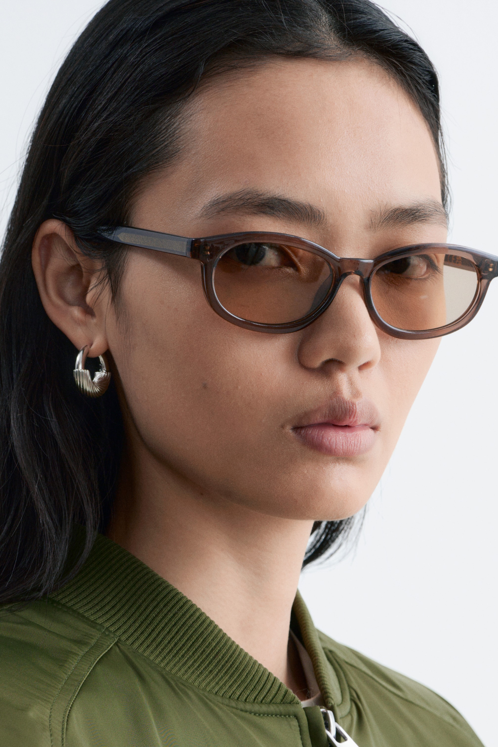 Ver imagem maior: Óculos de sol retangulares estreitos em castanho escuro com lentes de tonalidade castanha estão a ser usados pela modelo.