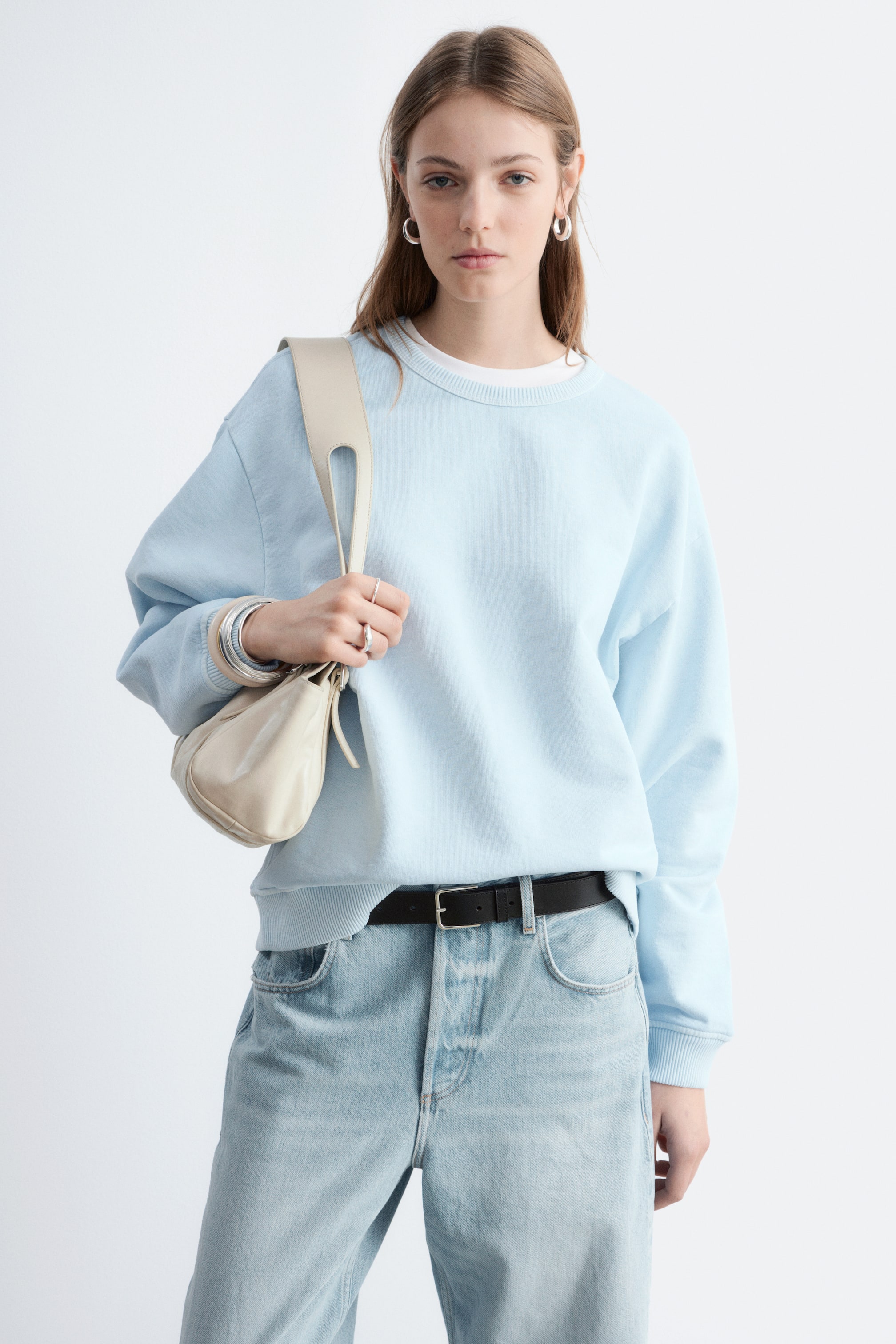 Se større billede: En lyseblå crewneck sweatshirt præsenteres fra en frontvendt vinkel, med en ribbet krave, ribbede manchetter og en ribbet kant, hvor en hvid t-shirt tydeligt kan ses lagret underneden.