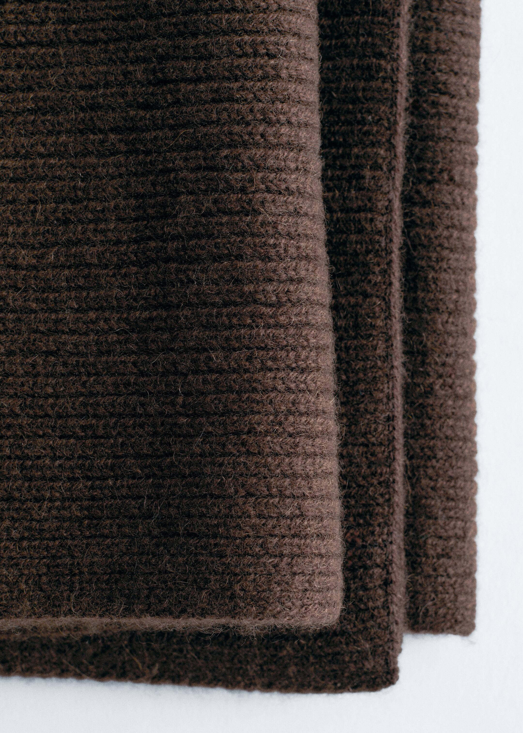 Agrandir l'image: Un tissu tricoté brun foncé est présenté, plié en plusieurs couches. La couche supérieure visible affiche un motif côtelé proéminent avec des lignes horizontales et une texture douce, légèrement duveteuse.