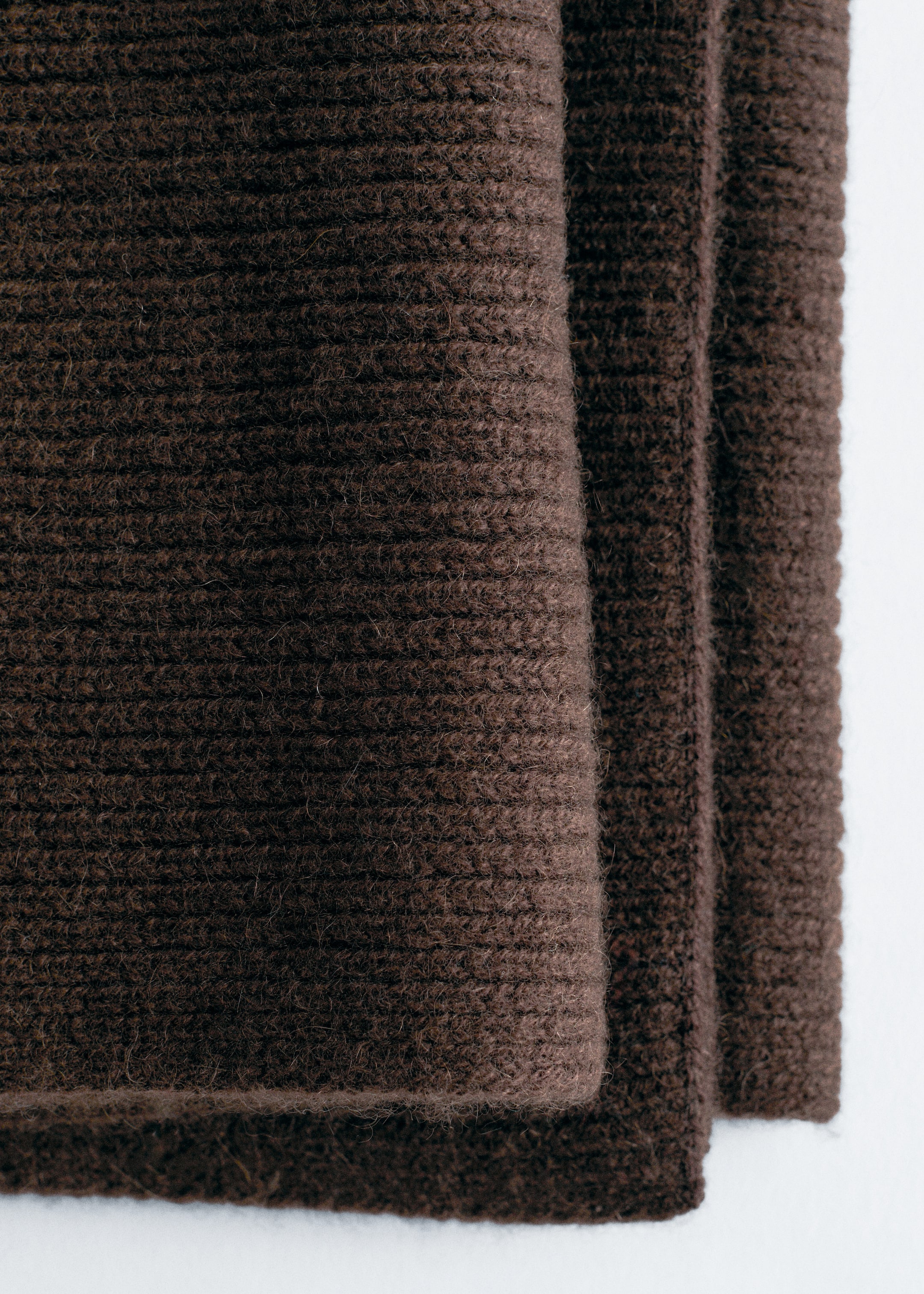 Grösseres Bild ansehen: Ein dunkelbrauner Strickstoff wird gezeigt, der in mehrere Lagen gefaltet ist. Die sichtbare obere Lage zeigt ein markantes Rippmuster mit horizontalen Linien und einer weichen, leicht flauschigen Textur.