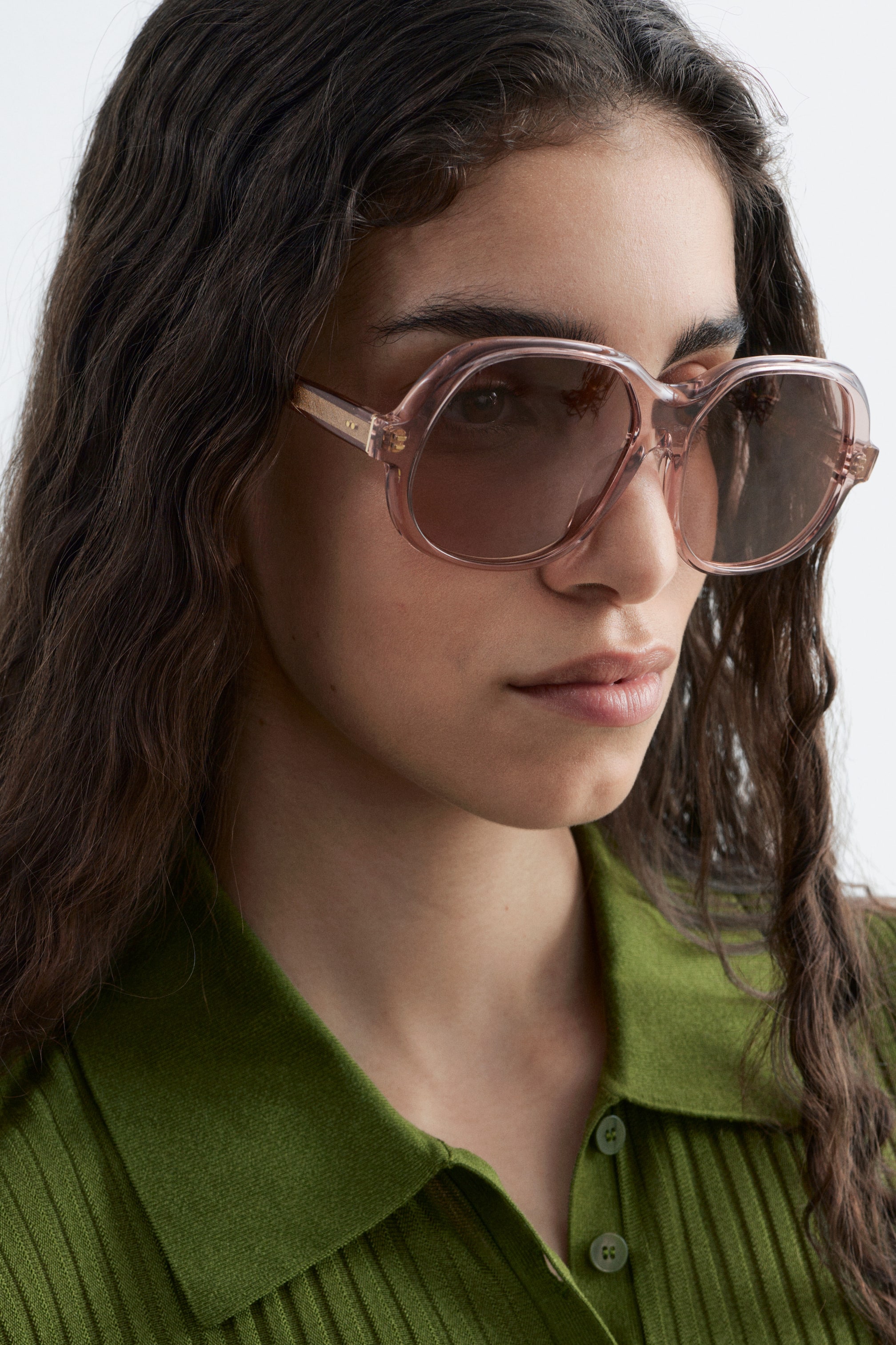 Visa större bild: Solglasögonen har överdimensionerade, genomskinliga rosa fyrkantiga-runda bågar med mörkt tonade linser. Guldfärgade detaljer syns på skalmarna, och solglasögonen bärs i en lätt trekvartsvinkel.