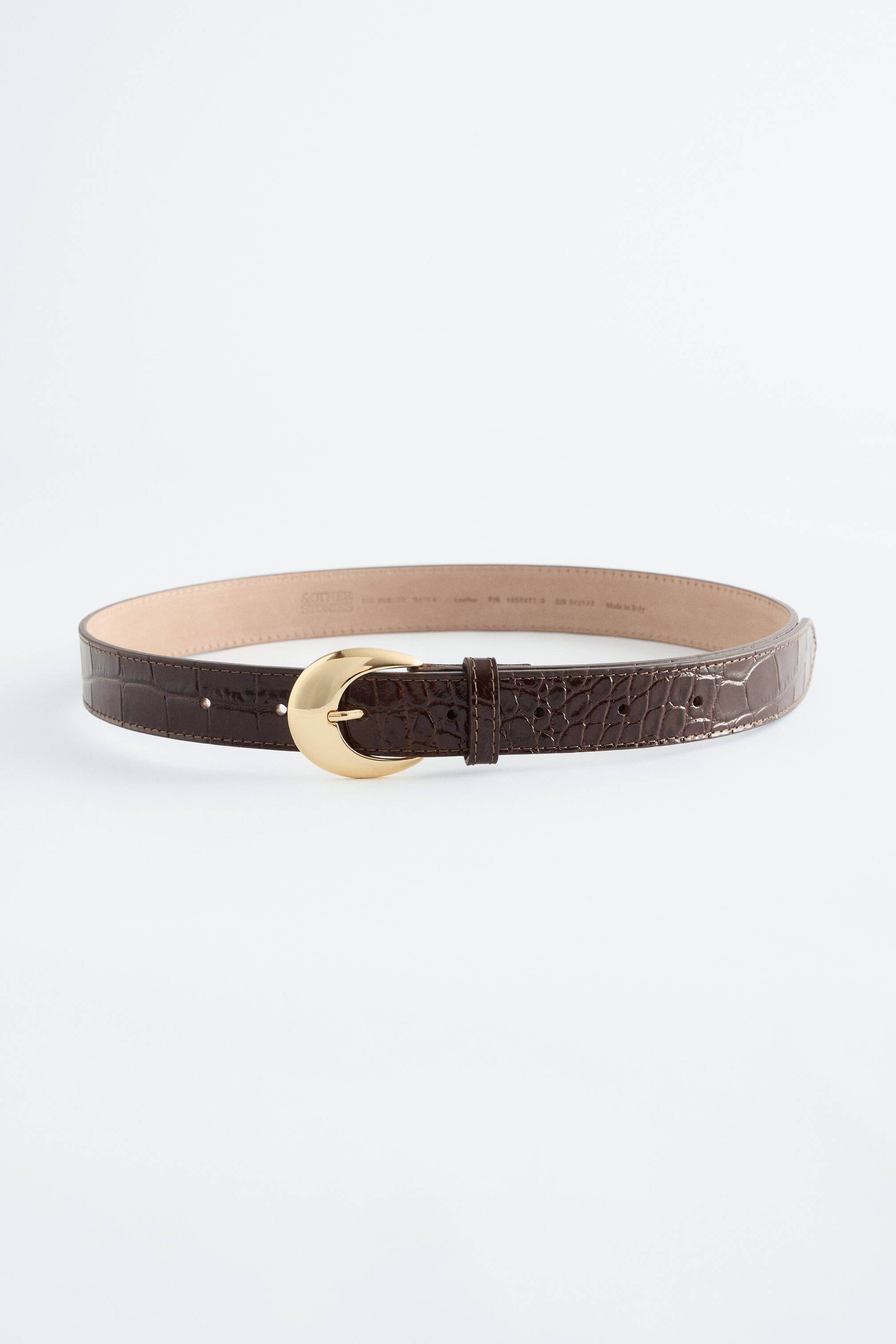 Visualizza immagine più grande: Una cintura in pelle marrone scuro con stampa effetto coccodrillo è mostrata leggermente curva, caratterizzata da una fibbia dorata lucida con una distintiva forma a mezzaluna sul davanti.