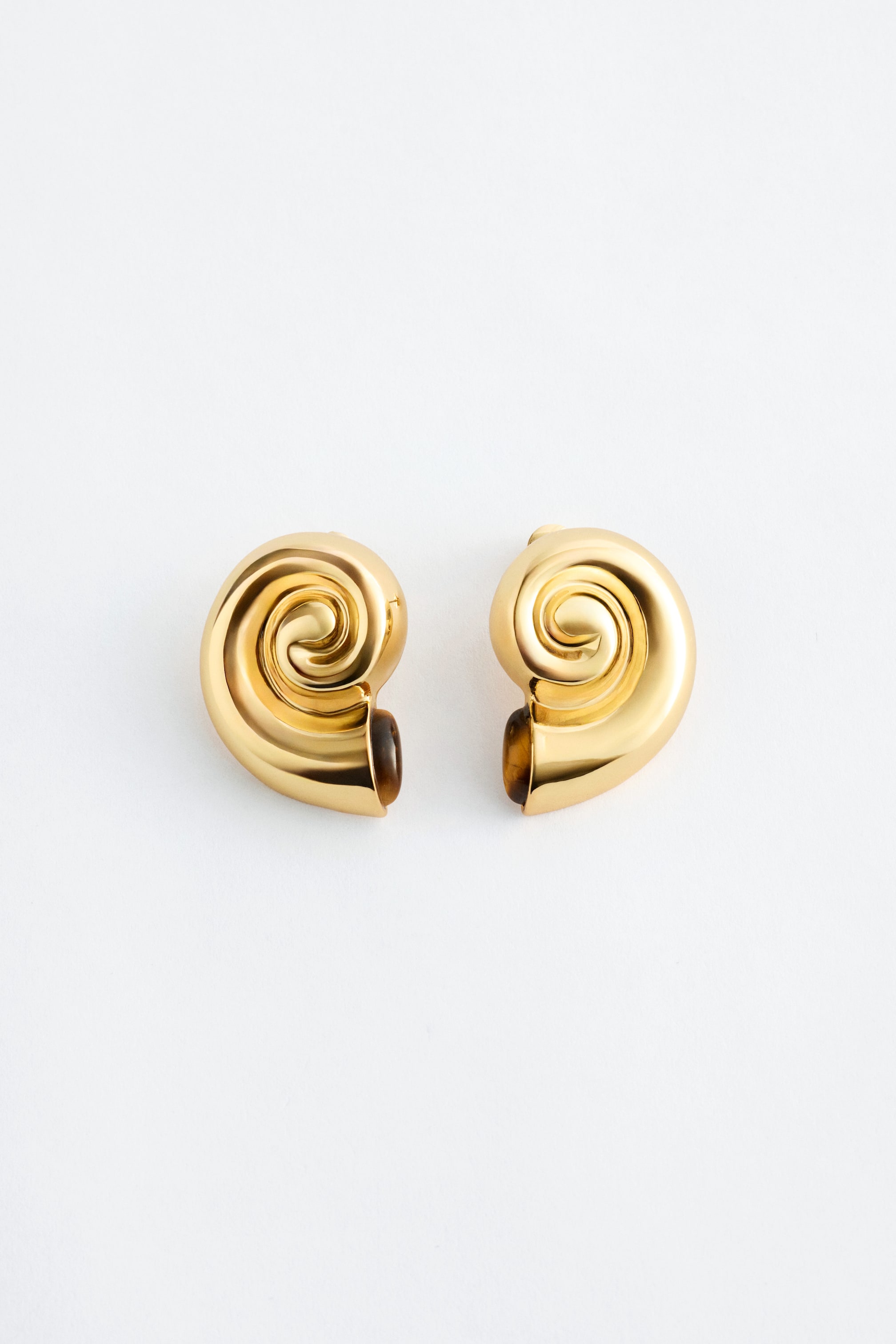 Größeres Bild anzeigen: Ein Paar goldfarbene Ohrringe präsentiert ein poliertes Spiraldesign, wobei jeder Ohrring an seiner gebogenen Basis ein dunkleres, kontrastierendes Inlay aufweist.