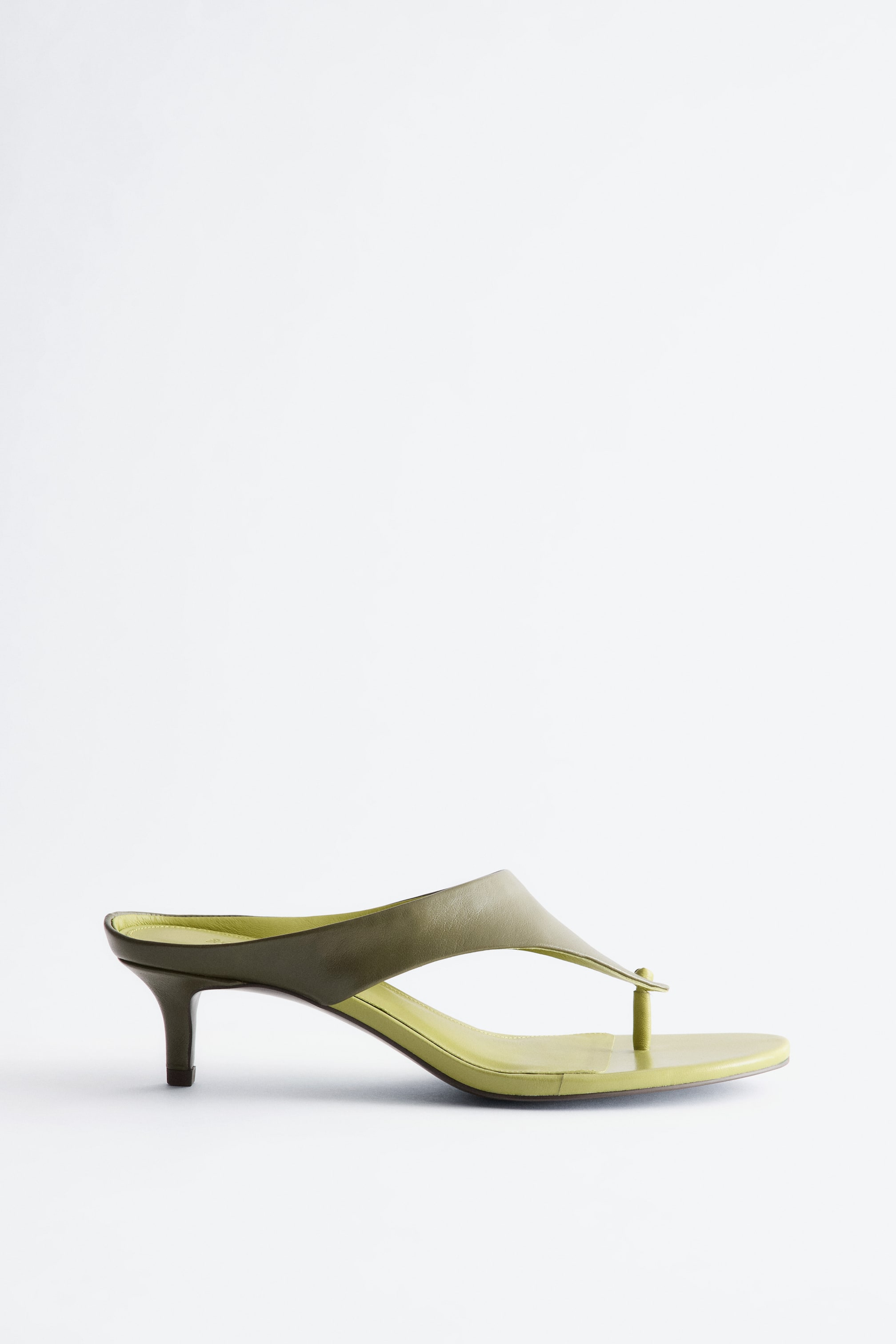 Agrandir l'image: Une mule à talon haut vert olive est orientée vers la gauche, affichant une large bride supérieure et un entre-doigt. Un talon aiguille soutient la chaussure, et une semelle intérieure vert clair est visible.