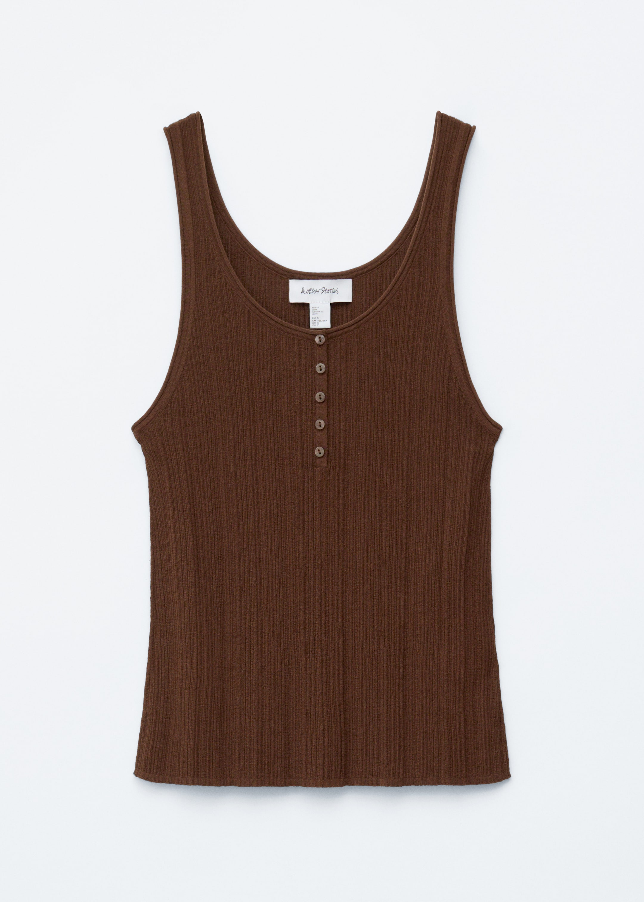 Se større billede: En brun tanktop er fint strikket i en ribbet tekstur, med en rund halsudskæring fremhævet af en halv stolpelukning med seks små brune knapper, og er afsluttet med blødt rullede, rørformede kanter langs halsudskæringen, ærmegabene og kanten.