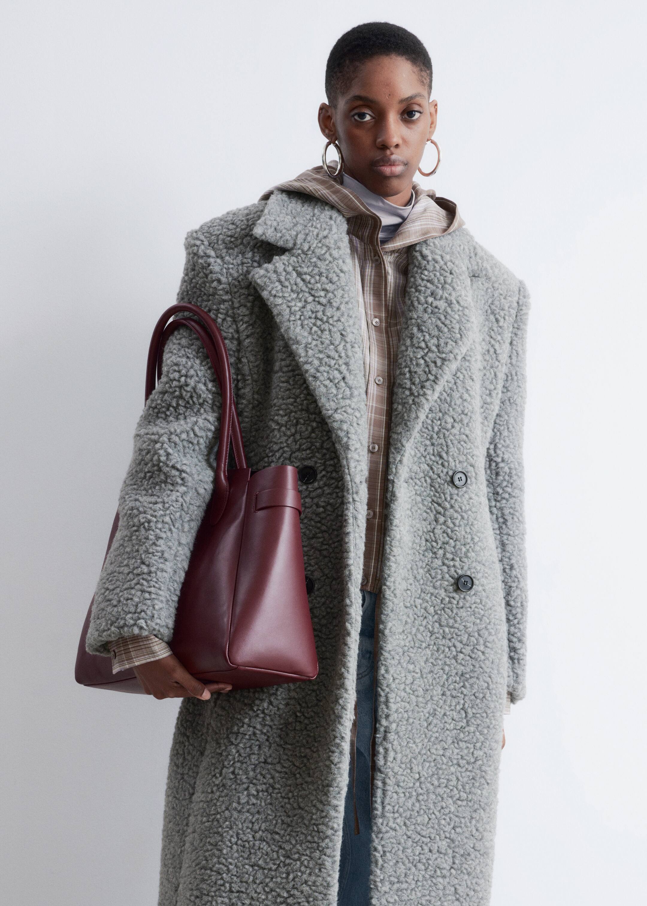 View larger image: A gray, shaggy teddy coat is being worn, featuring notch lapels and a double-breasted style with two visible dark buttons, and is layered over a plaid shirt.