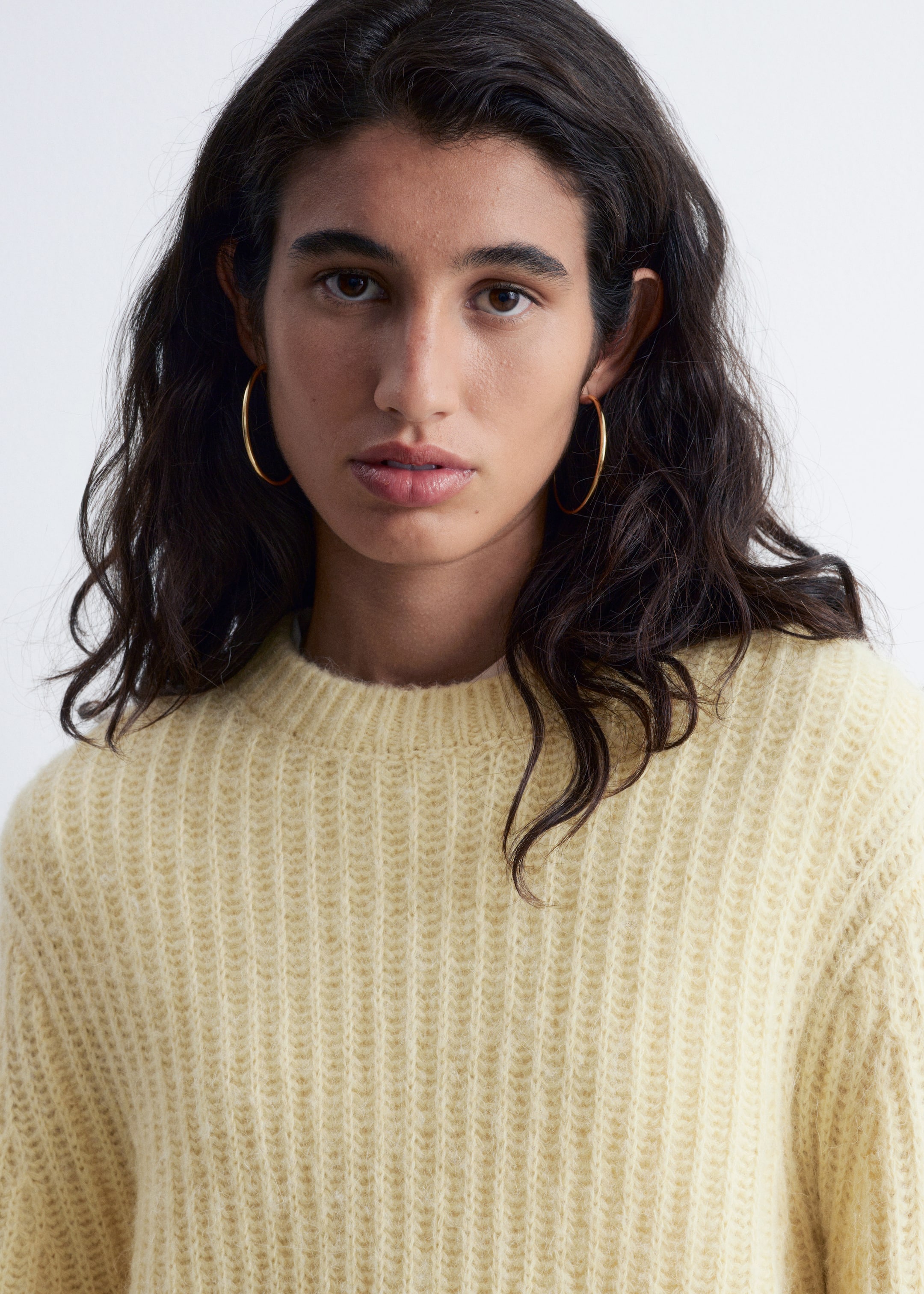 Visualizza immagine più grande: Un maglione giallo chiaro con scollo a girocollo viene indossato, visto dal petto in su, mettendo in risalto il suo ampio motivo a coste e la sua texture pelosa.