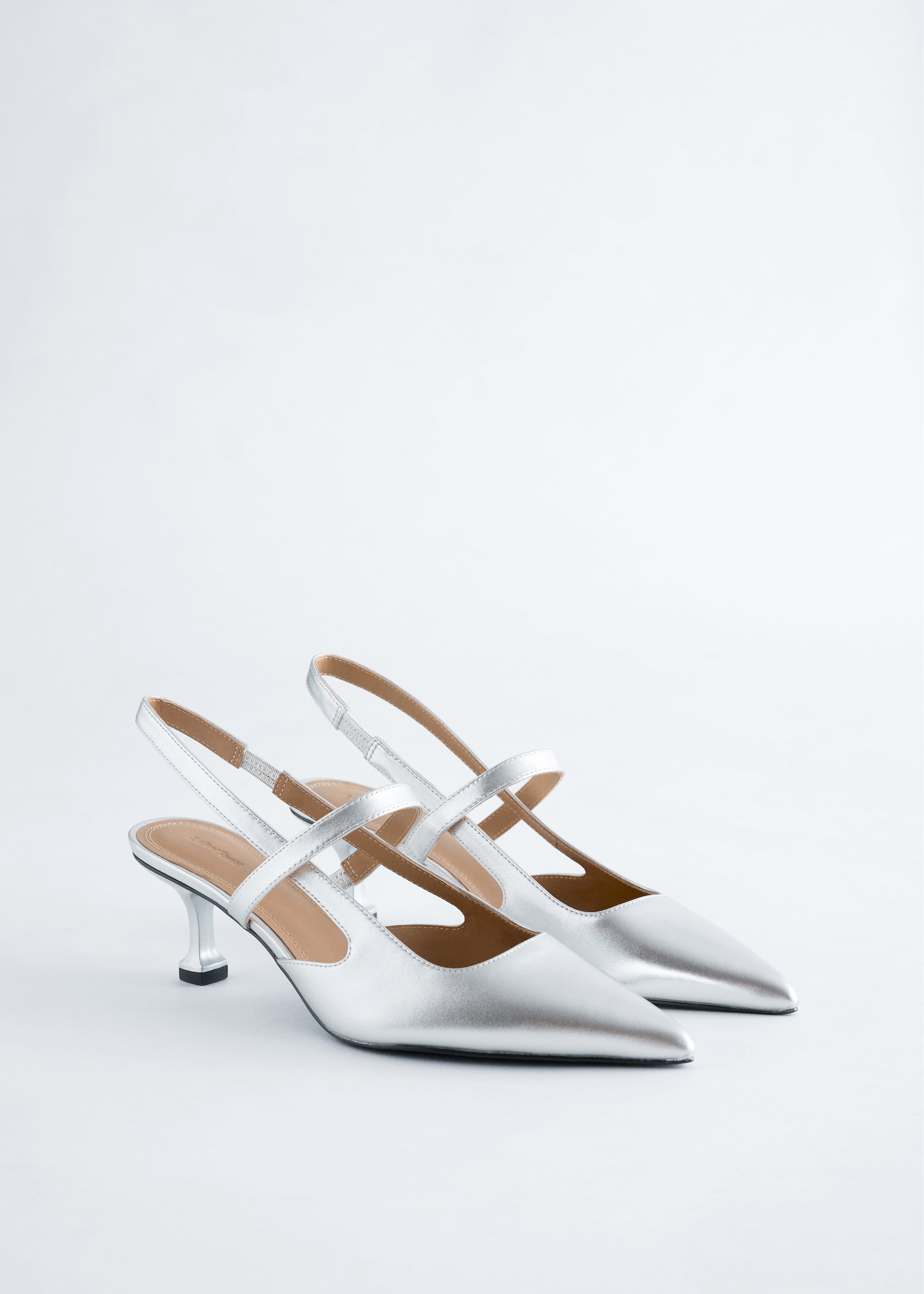 Agrandir l'image: Une paire d'escarpins slingback argentés est présentée, avec des bouts pointus, deux brides horizontales croisées sur le cou-de-pied, et un talon aiguille évasé. Les chaussures sont orientées vers la gauche, montrant leur finition métallique.
