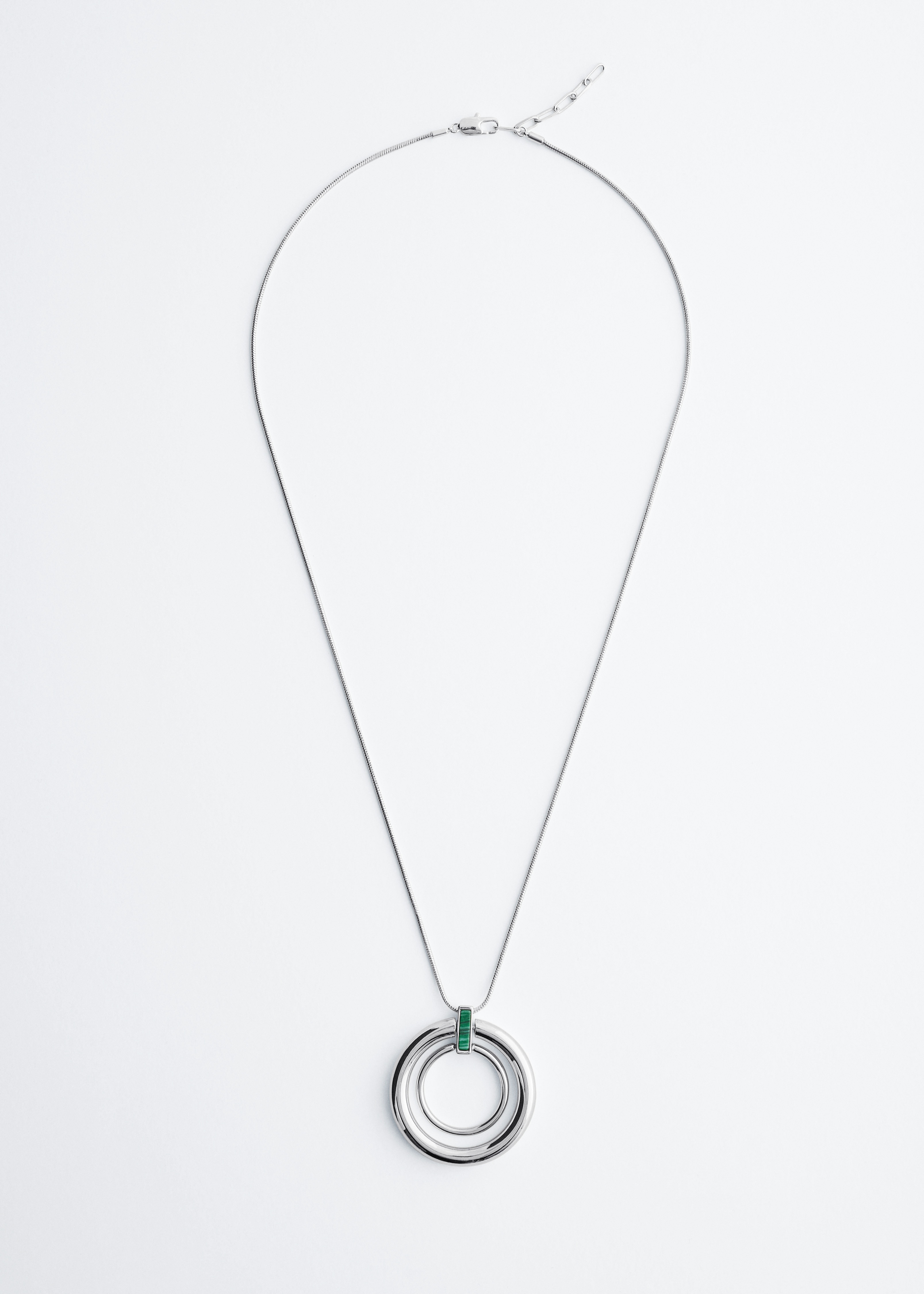 A grey brushed cashmere V-neck jumper is being worn by the model, styled with a polished snake chain necklace featuring a double-circle pendant joined by a rectangular accent. The necklace rests against the modelâs chest, showcasing its metallic finish against the soft texture of the jumper.