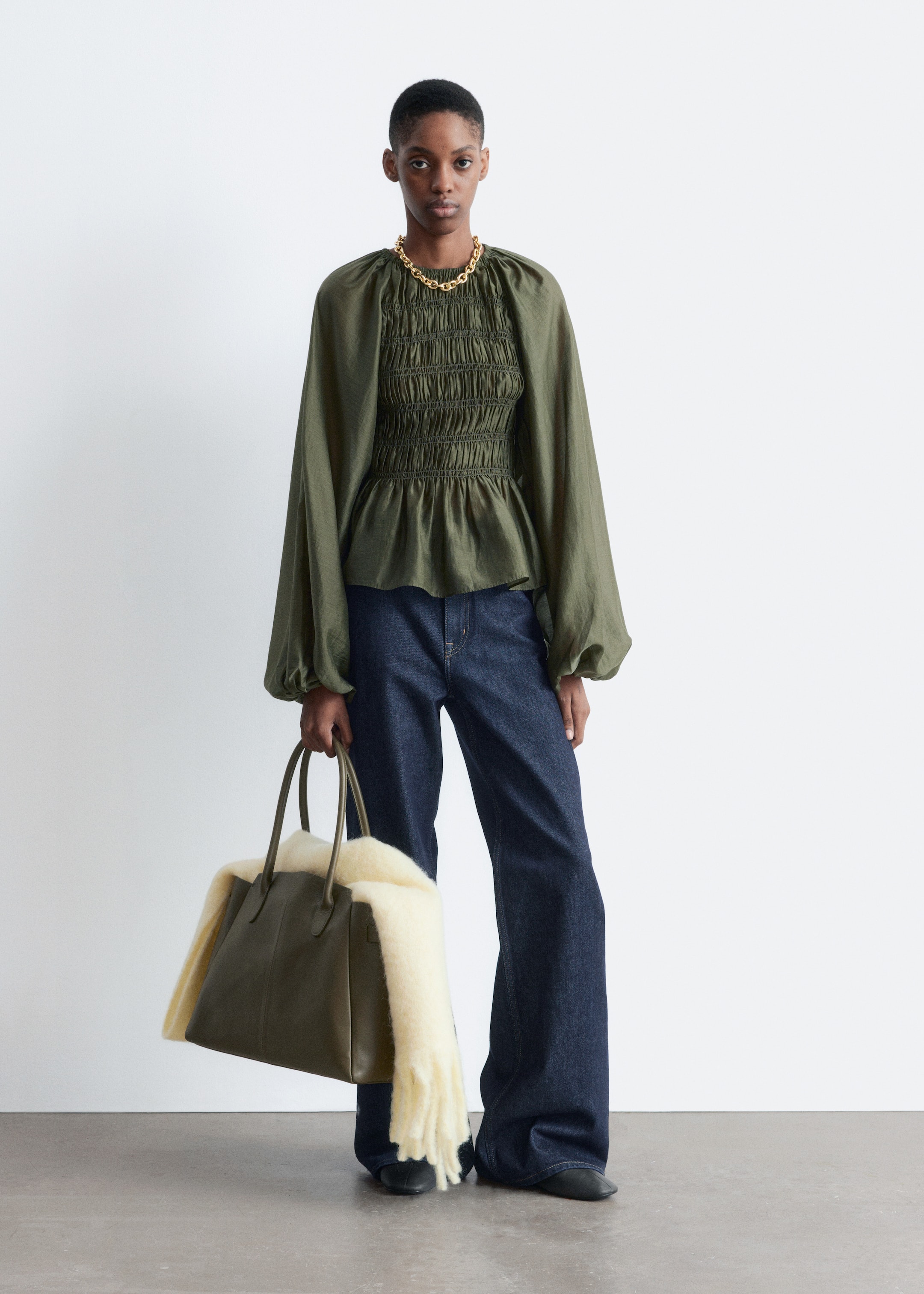 View larger image: An olive green top is featuring a gathered round neckline, extensive smocking across the bust and mid-torso, and long, voluminous sleeves with gathered cuffs. A peplum hem is flaring out below the smocked section.
