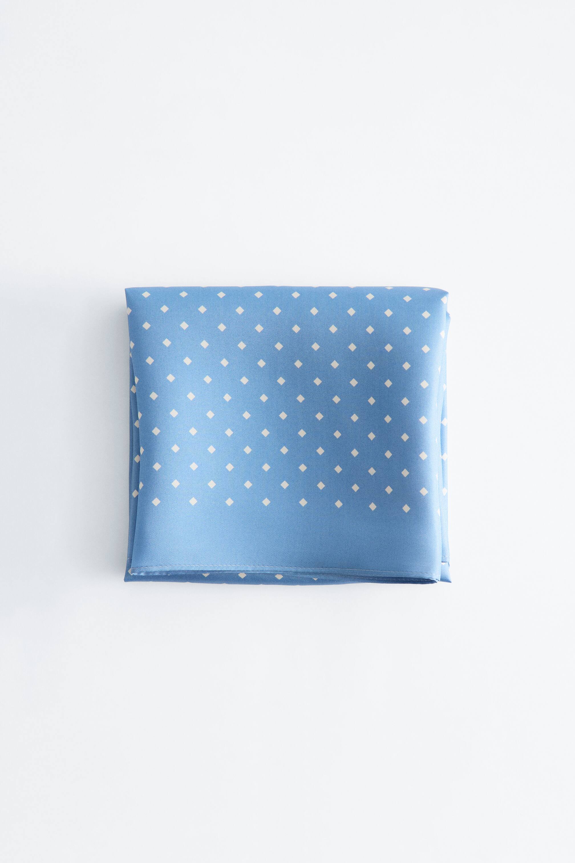 Größeres Bild ansehen: Ein blauer Schal ist zu einem Quadrat gefaltet und zeigt ein sich wiederholendes Muster aus kleinen, cremefarbenen Diamantpunkten.
