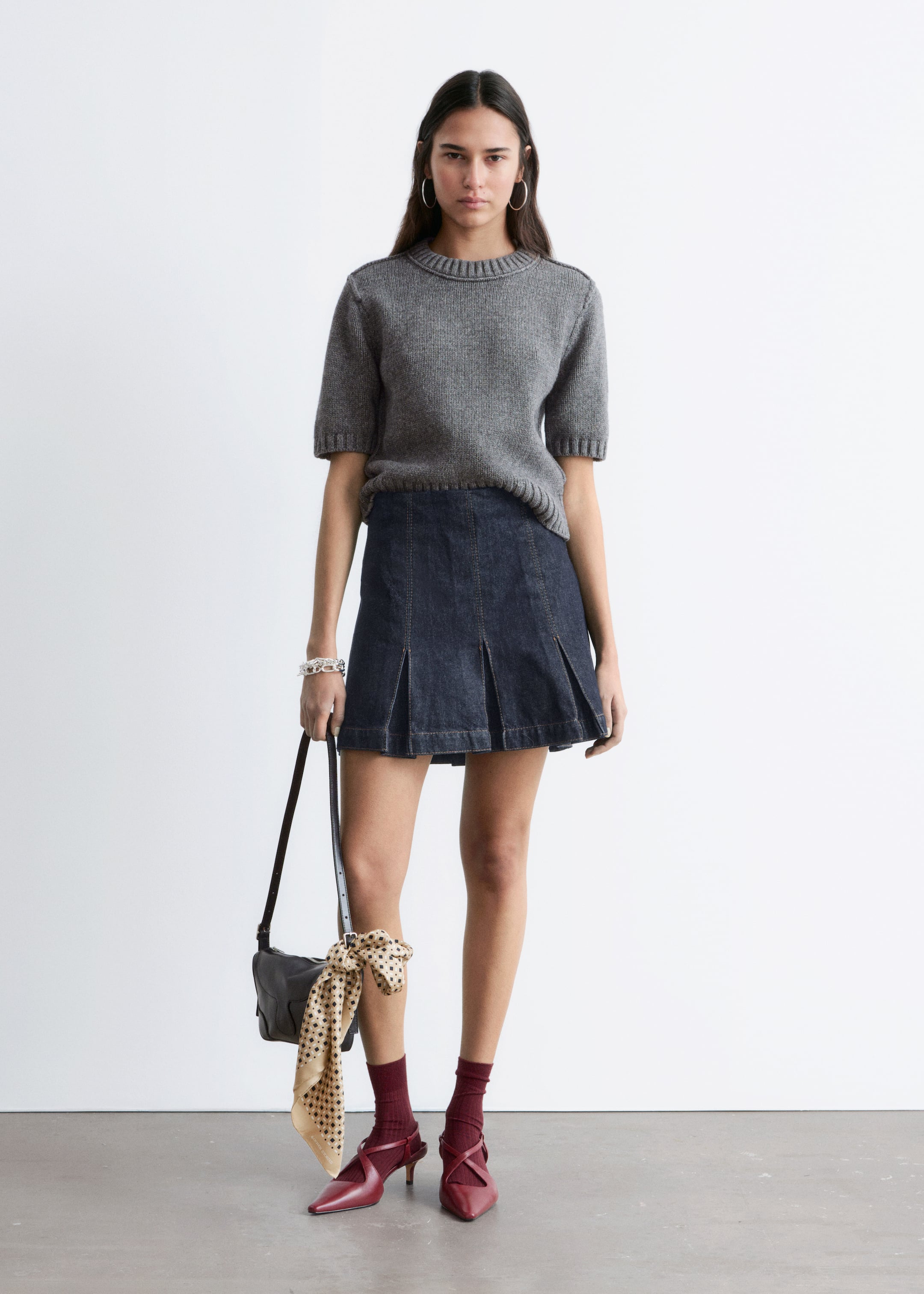 Προβολή μεγαλύτερης εικόνας: Ένα γκρι πλεκτό πουλόβερ με κοντά μανίκια διαθέτει ριγέ λαιμόκοψη, ριγέ μανσέτες και ριγέ τελείωμα, στυλιζαρισμένο πάνω από μια σκούρα τζιν μίνι φούστα σε απόχρωση του σκούρου ίντιγκο, που παρουσιάζει σχεδιασμό με πολλές κάθετες πιέτες ραμμένες στο μπροστινό μέρος.