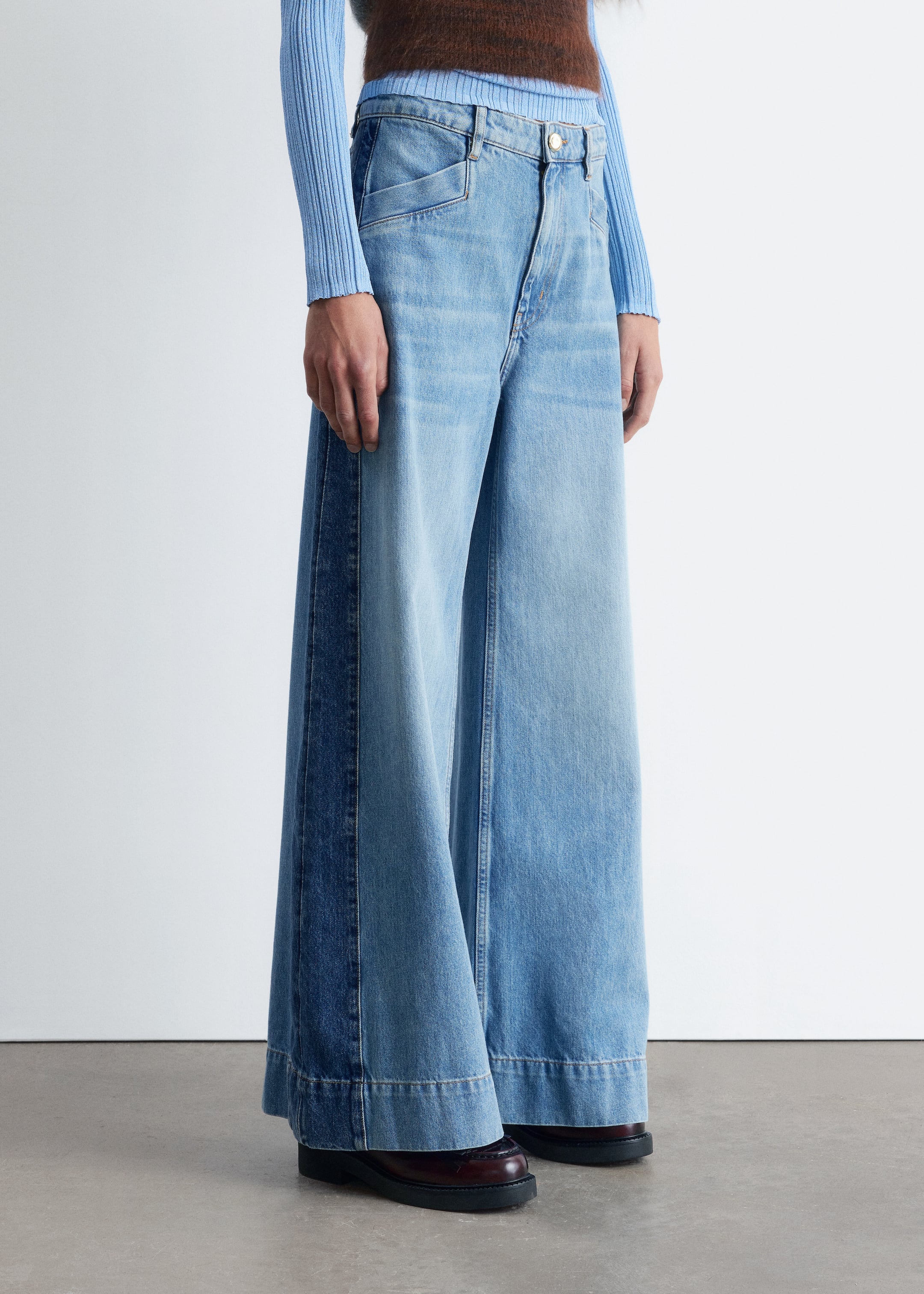 Größeres Bild ansehen: Hoch taillierte, hellblaue Jeans mit einer weiten, langen Silhouette werden von dem Model getragen, das auch ein hellblaues Oberteil trägt. Die Jeans haben dunklere Seitenpaneeldetails und einen breiten, abgesteppten Saum, wobei die zusätzliche Länge über dunklen Schuhen zusammenfällt.