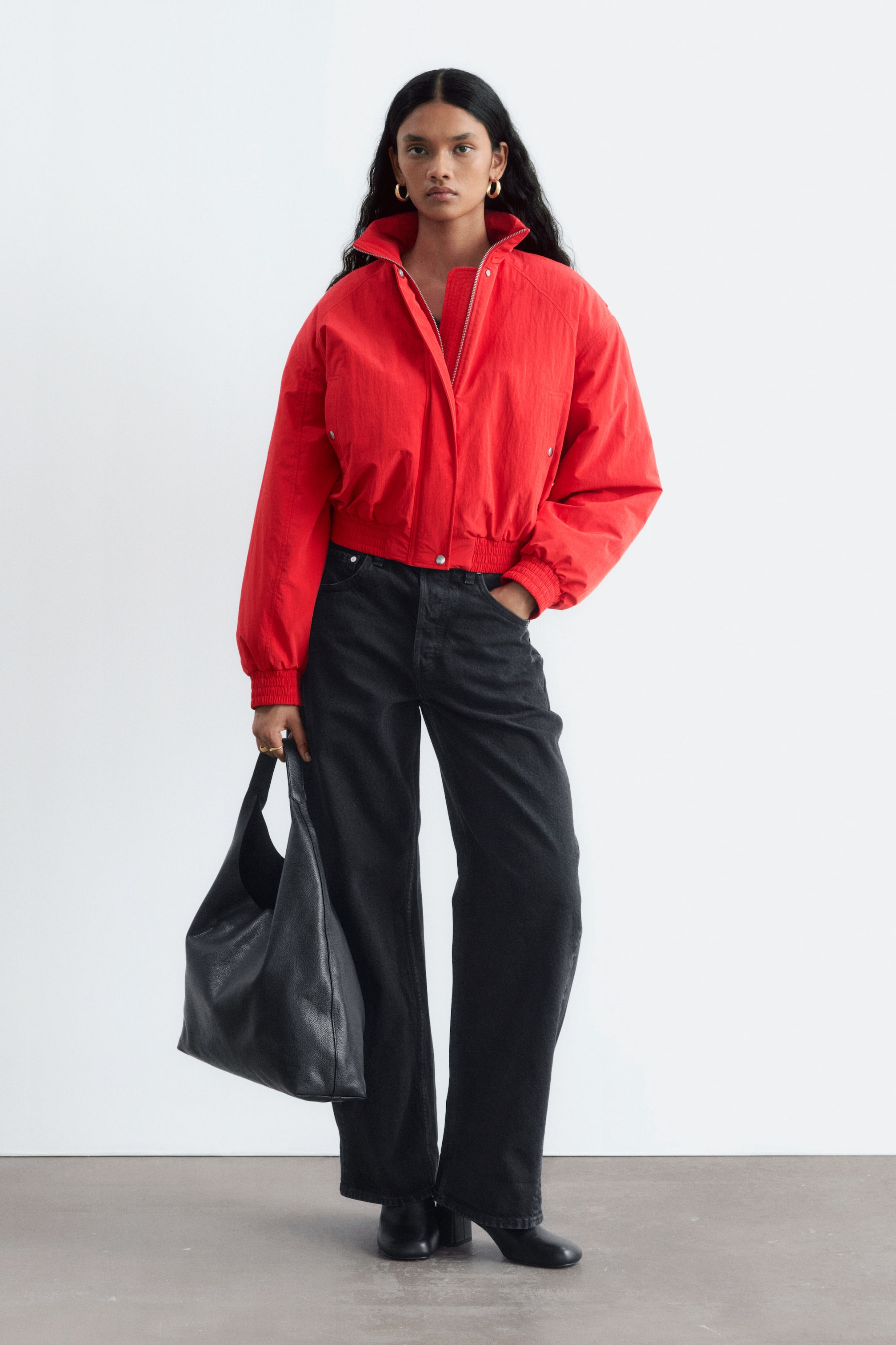 Vezi imaginea mai mare: Un bomber sport roșu, matlasat, cu mâneci raglan, plachetă frontală, manșete elastice și tiv elastic, este purtat de model. Jacheta este descheiată parțial cu fermoarul, dezvăluind un top roșu dedesubt.