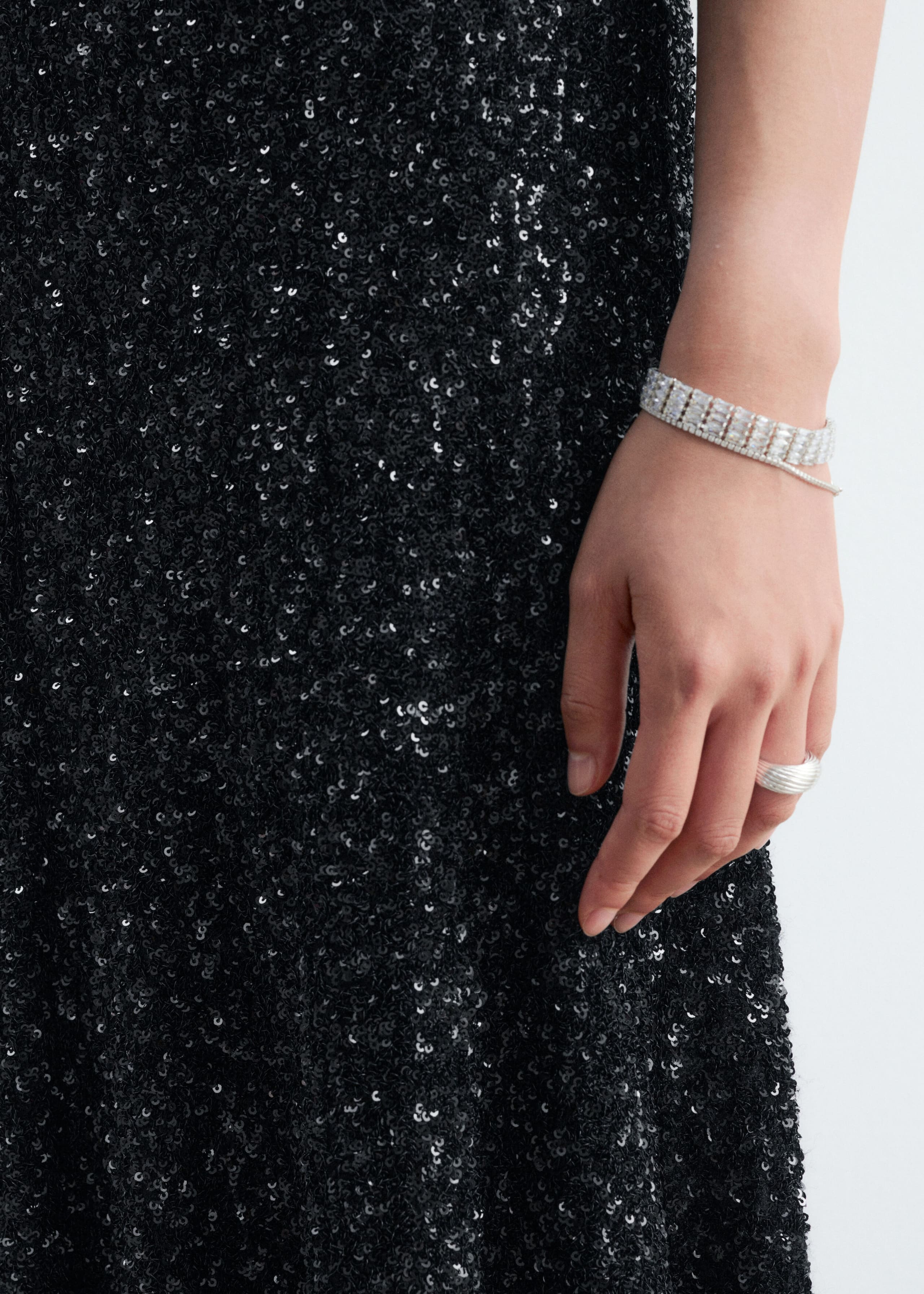 The model is wearing a black sequined mesh skirt and a silver-toned bracelet on her wrist, composed of repeating rows of cubic zirconia links.