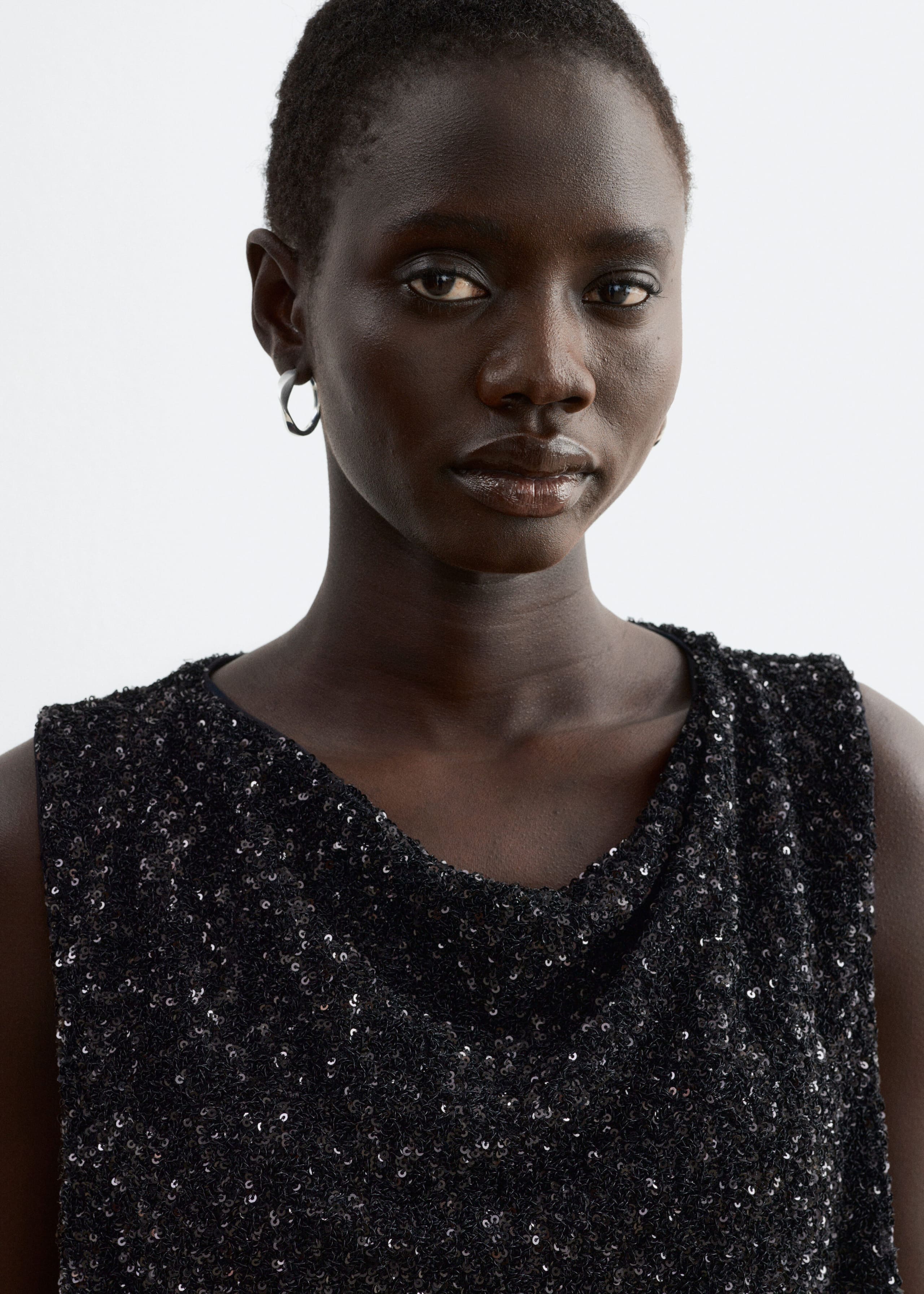 The model is wearing a black sleeveless top featuring all-over sequins and a draped neckline.