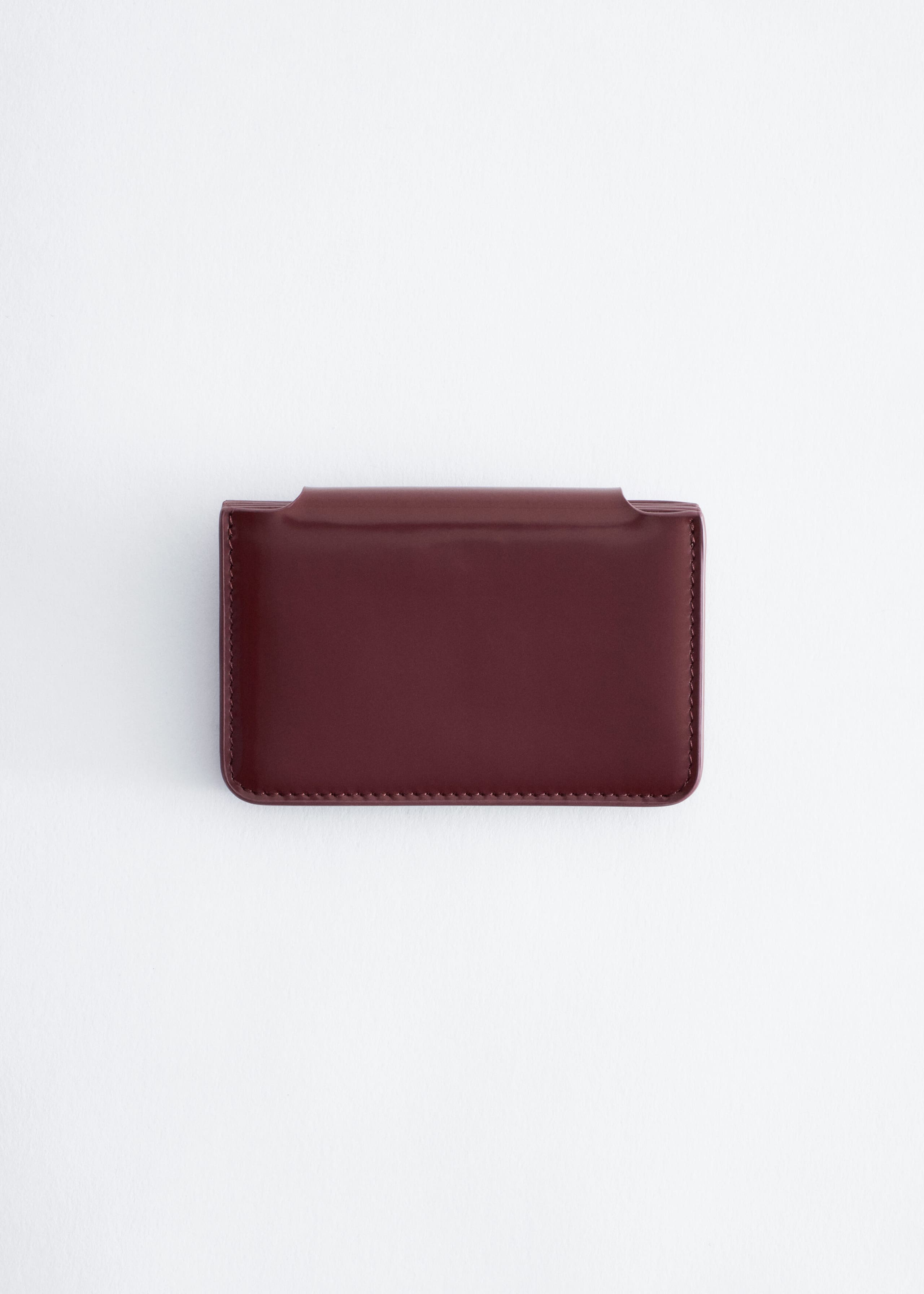 A dark burgundy leather card holder is shown from the back, highlighting its structured silhouette, smooth matte finish, and tonal stitching along the edges.