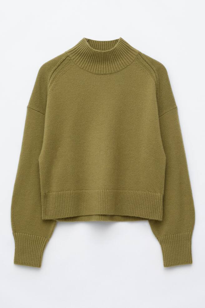 Un pull col montant en maille vert olive est prÃ©sentÃ© de face, avec une coupe dÃ©contractÃ©e, des Ã©paules tombantes et des coutures dâÃ©paules avancÃ©es. Ce pull en maille prÃ©sente un col montant cÃ´telÃ©, des manches longues avec poignets cÃ´telÃ©s et un large ourlet cÃ´telÃ©. - 1