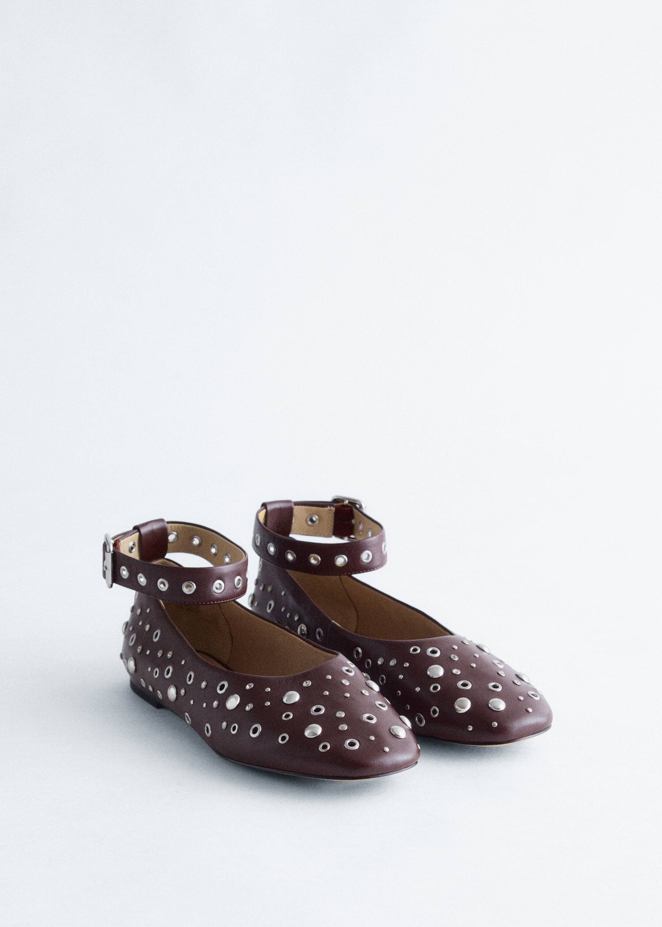 View larger image: A pair of dark red leather ballerinas is being presented, angled slightly from the front. The shoes are adorned with numerous scattered flat silver-tone studs and eyelets across the toe box and sides, and wide, matching leather ankle straps with silver-tone buckles and eyelets are attached and standing upright.