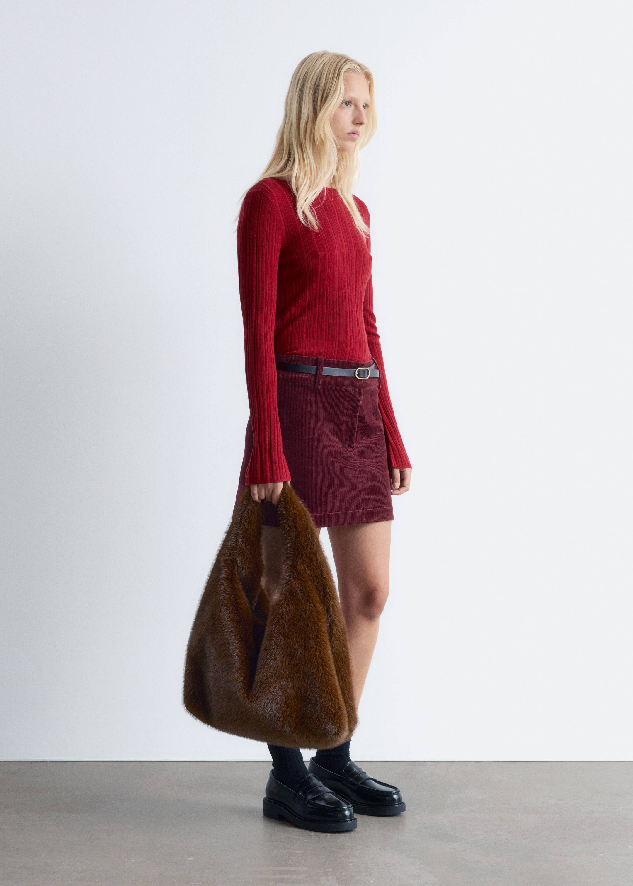 Agrandir l'image: Un haut en tricot côtelé rouge est présenté de profil, tourné vers la droite. Il présente un col rond et des manches longues, et est stylé dans une coupe ajustée, rentré dans une jupe en velours côtelé bordeaux.