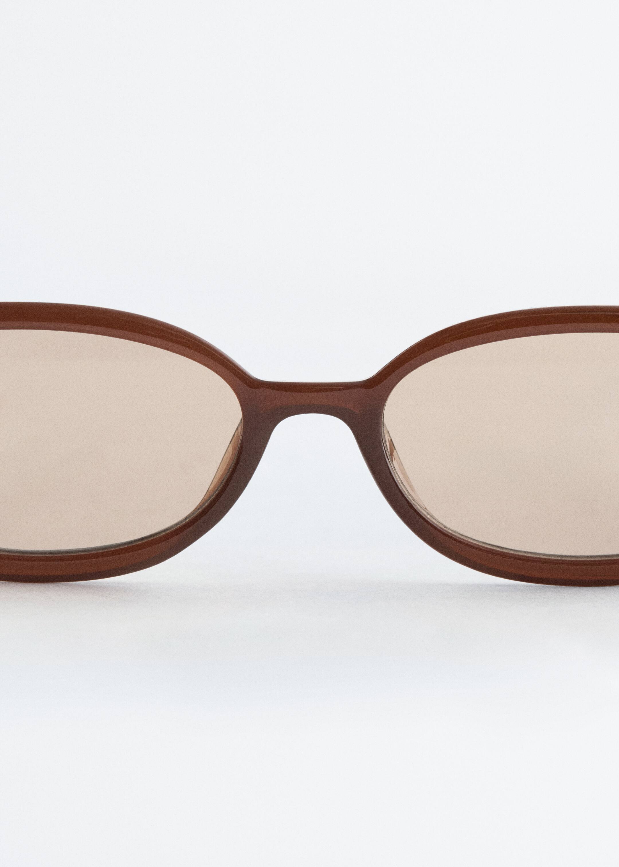 Vis større bilde: Brune solbriller presenteres Foran, med en skinnende, liten oval ramme og tonet lysebrune glass.