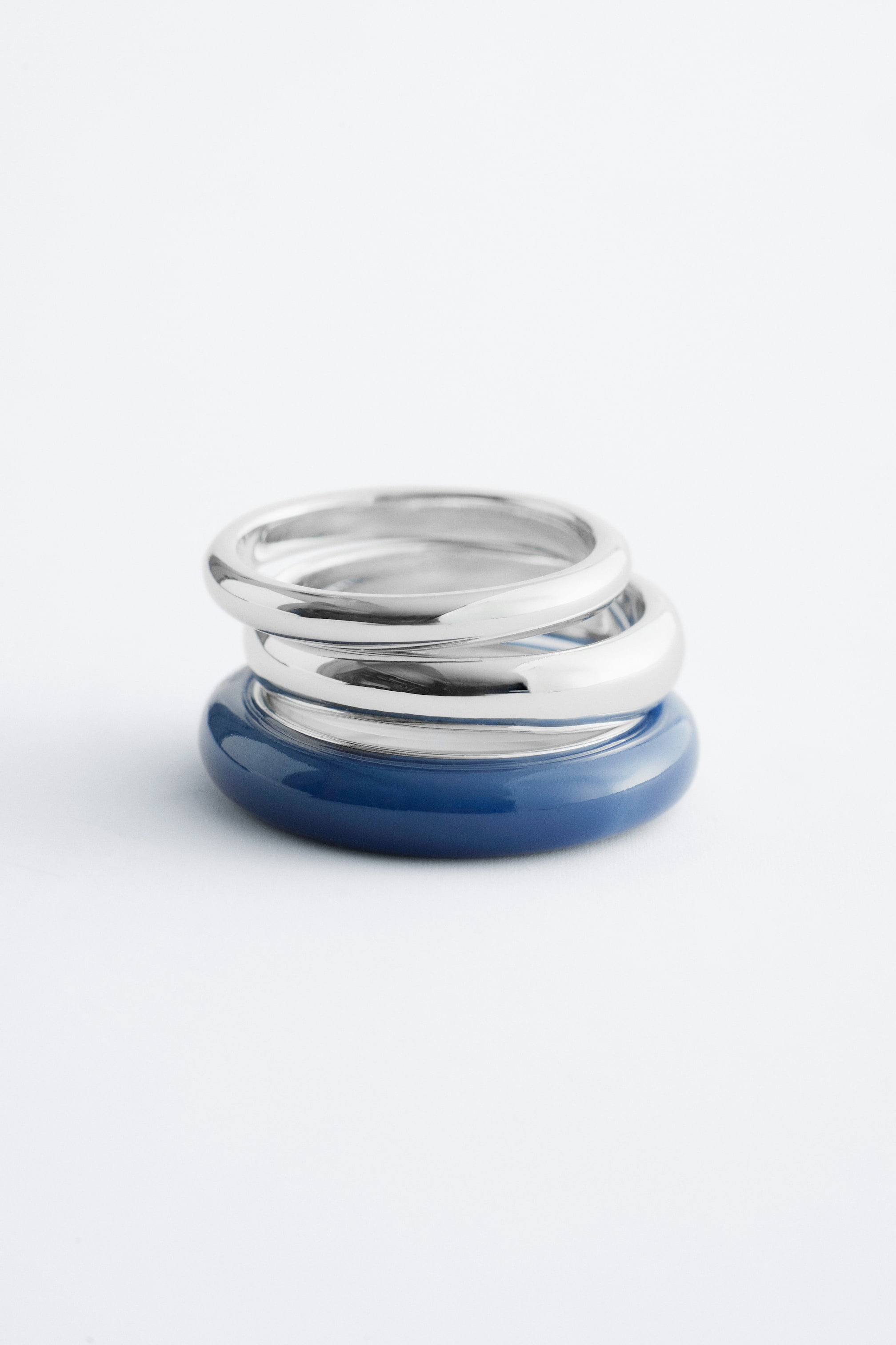 Größeres Bild anzeigen: Drei glatte, abgerundete Ringe stapeln sich und präsentieren zwei metallisch silberfarbene Bänder mit hochglänzendem Finish, die auf einem glänzenden dunkelblauen Band ruhen.