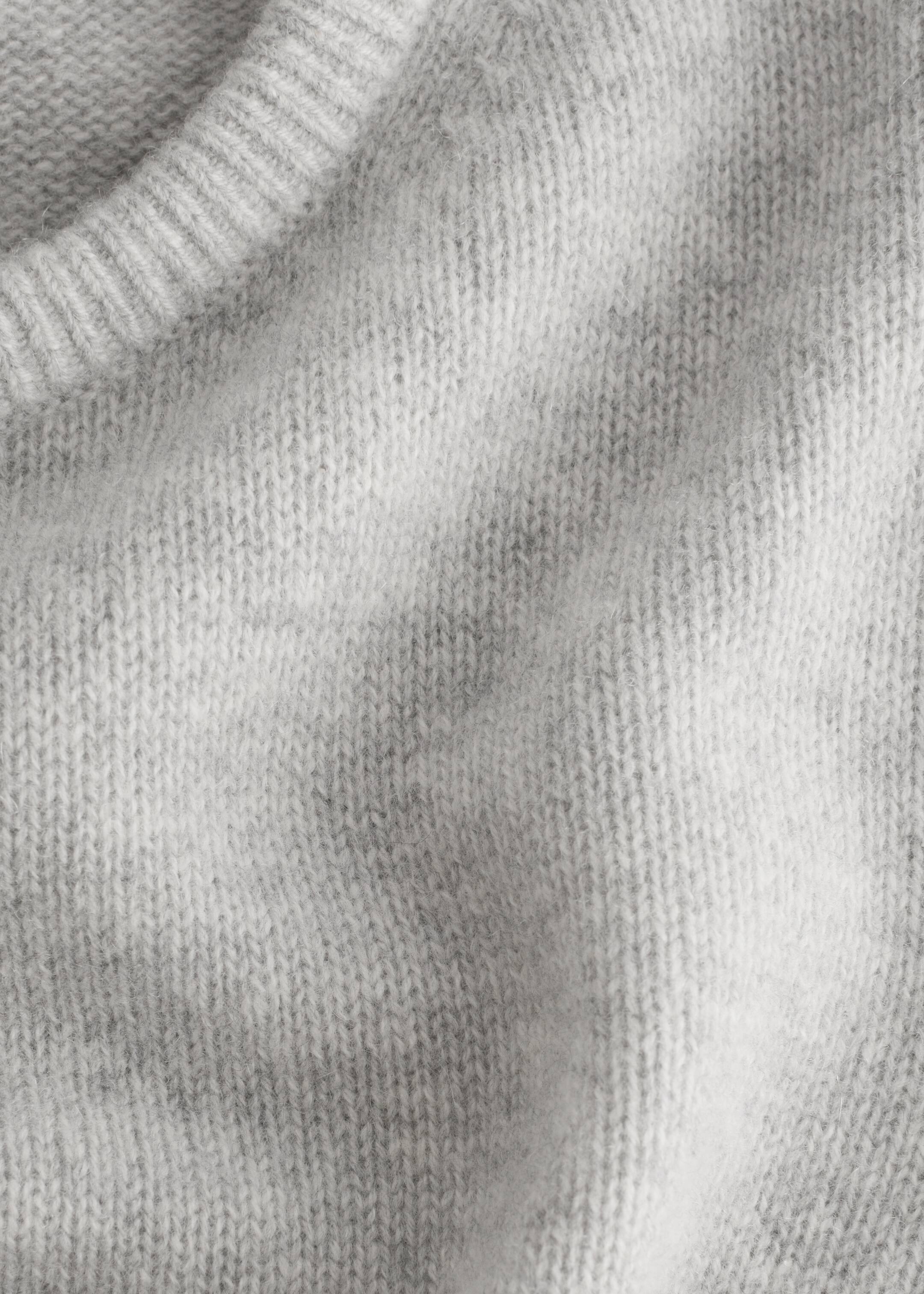 Vezi imaginea mai mare: Un prim-plan al unui tricou tricotat de culoare gri deschis arată un tiv ribat și un corp texturat. Materialul prezintă un model tricotat vizibil și o suprafață ușor pufoasă.