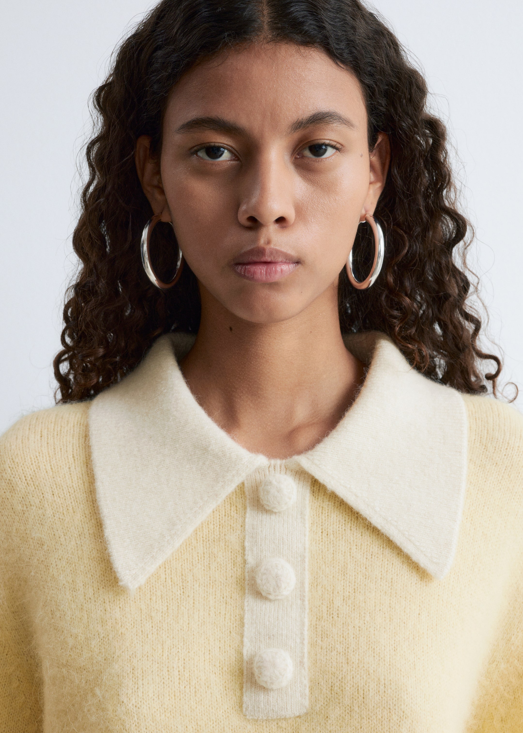 View larger image: A light yellow knitted sweater is shown from the front, featuring a contrasting cream-colored spread collar. The sweater is displaying a button placket with three spherical cream buttons and a soft, fuzzy texture.