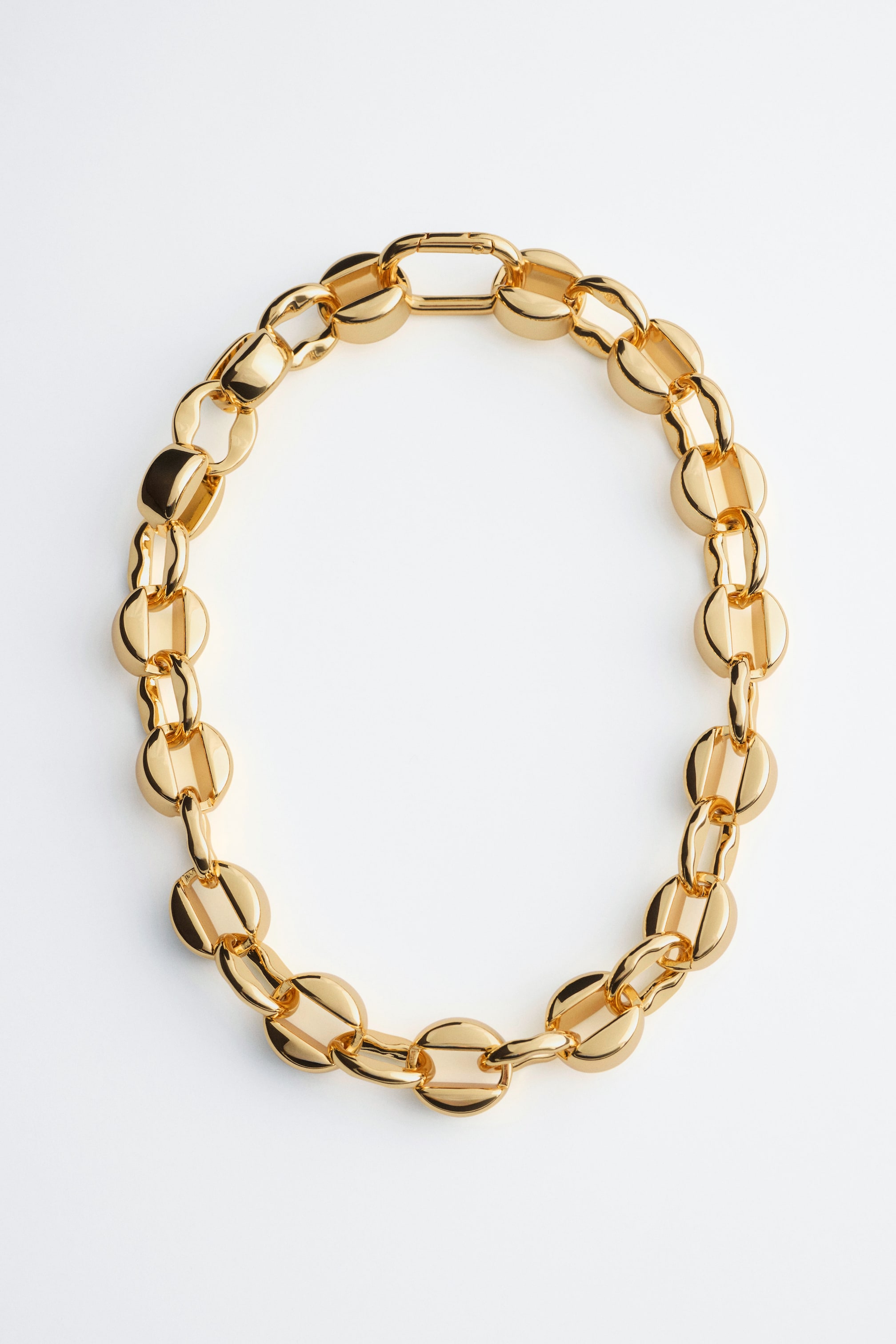 Visualizza immagine più grande: Una collana a catena color oro è adagiata piatta in forma ovale, con maglie spesse e arrotondate, caratterizzate da una finitura altamente lucida e riflettente. La vista frontale ne mette in evidenza la texture liscia e metallica e una chiusura rettangolare sicura nella parte superiore.