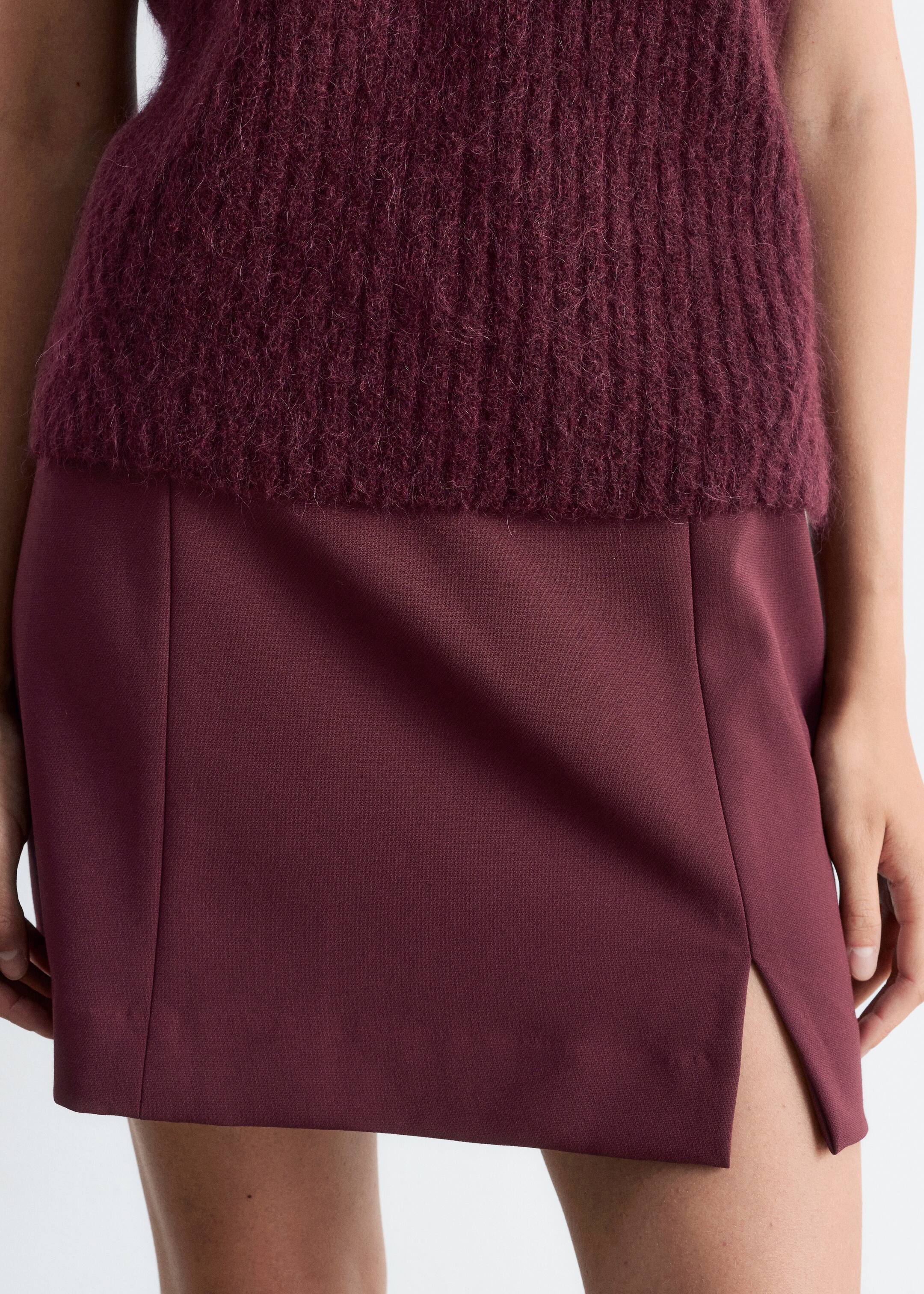 View larger image: A dark red, fuzzy knit top with visible vertical ribbing is being worn, layered over a matching dark red mini skirt. The skirt is featuring a smooth fabric and an angled side slit on the wearer's right leg.