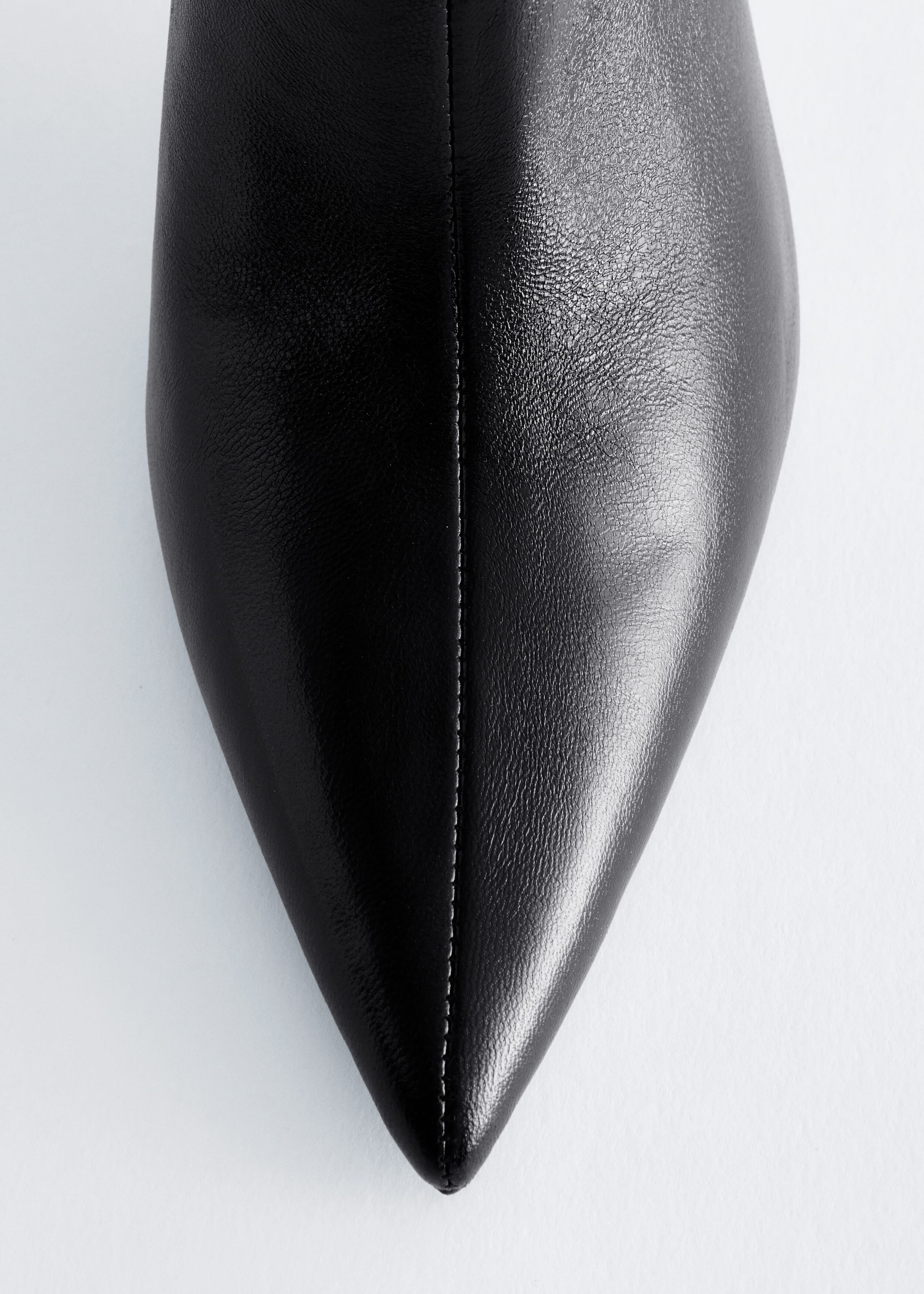 A black leather boot, viewed from above, showcases its sharp pointed toe and smooth, fine-grained texture. A prominent vertical seam runs down the centre of the upper, highlighting the boot's sleek, structured design.