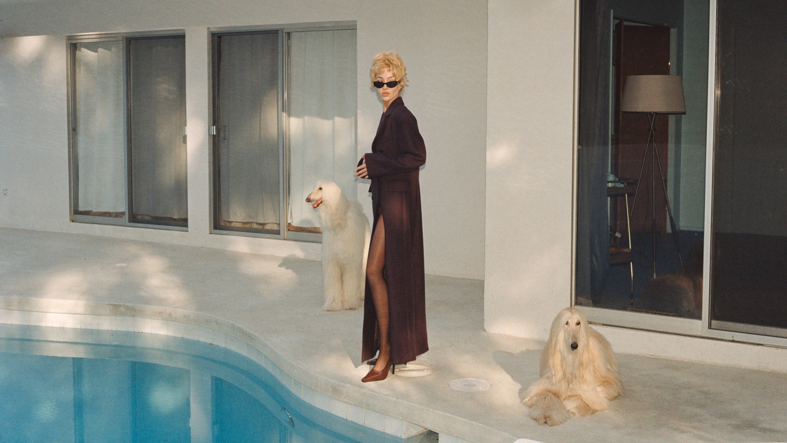 Woman in burgundy long coat by pool with two dogs